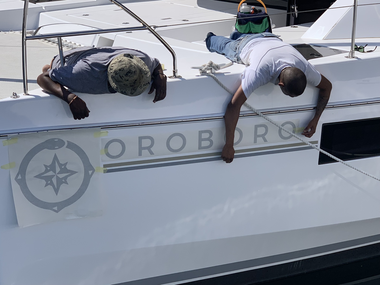Two craftsmen carefully applying the Oroboro name and logo to the hull