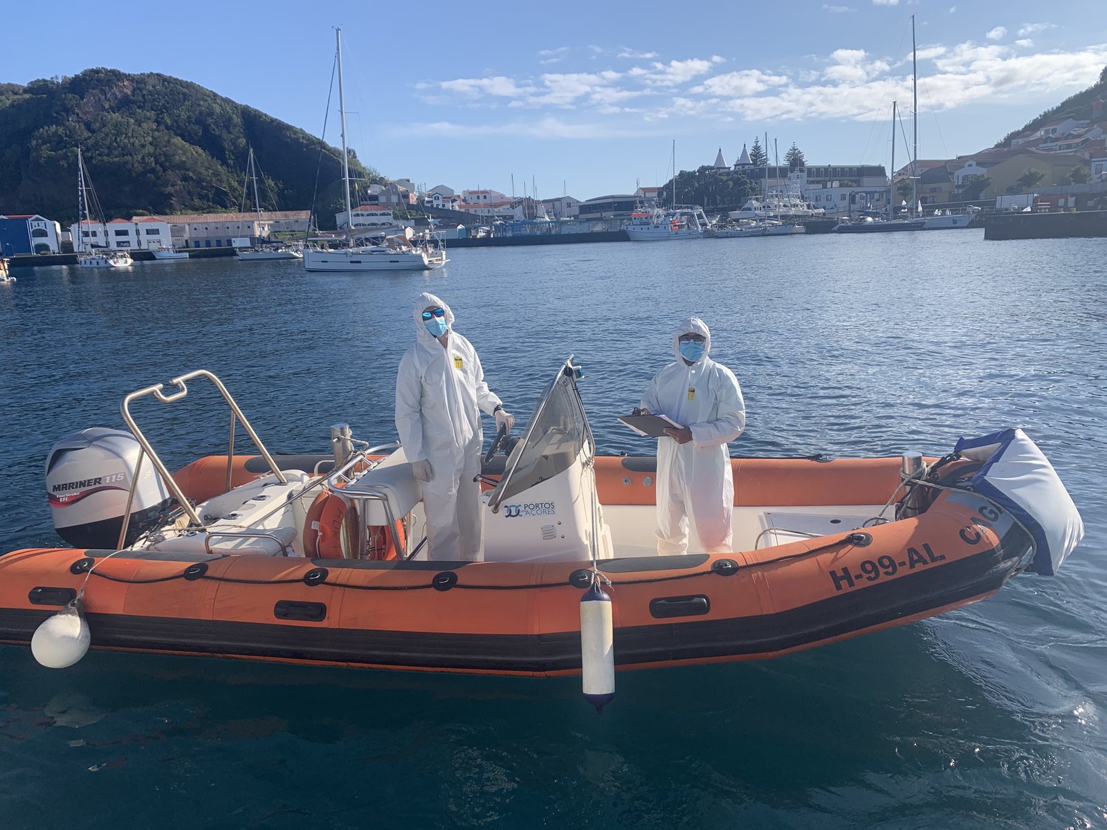 The COVID check-in crew alongside Oroboro — full PPE on an orange dinghy in the Atlantic.