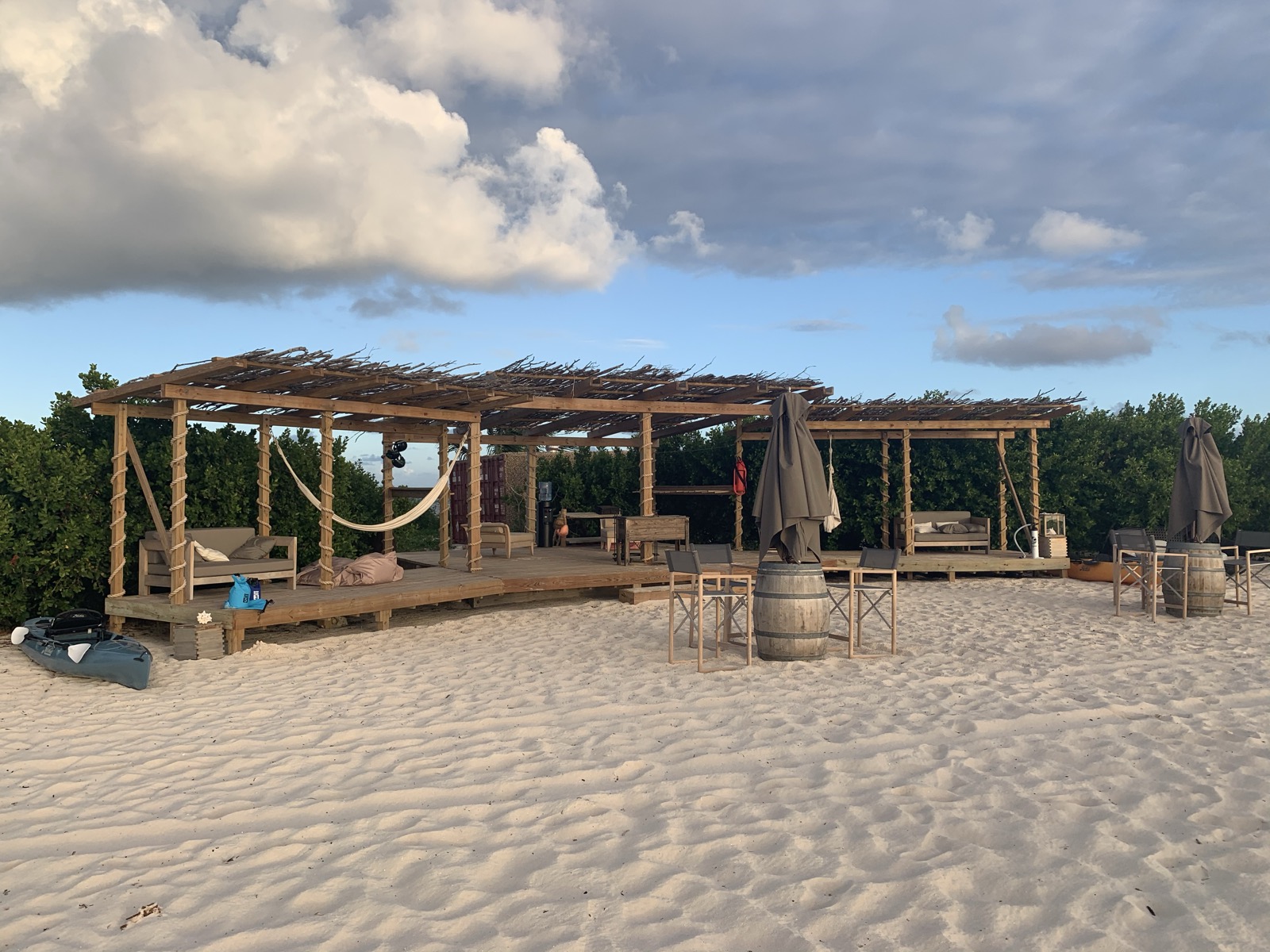 Barbuda's open-air beach bar — thatched pergola, hammock, barrel tables on white sand