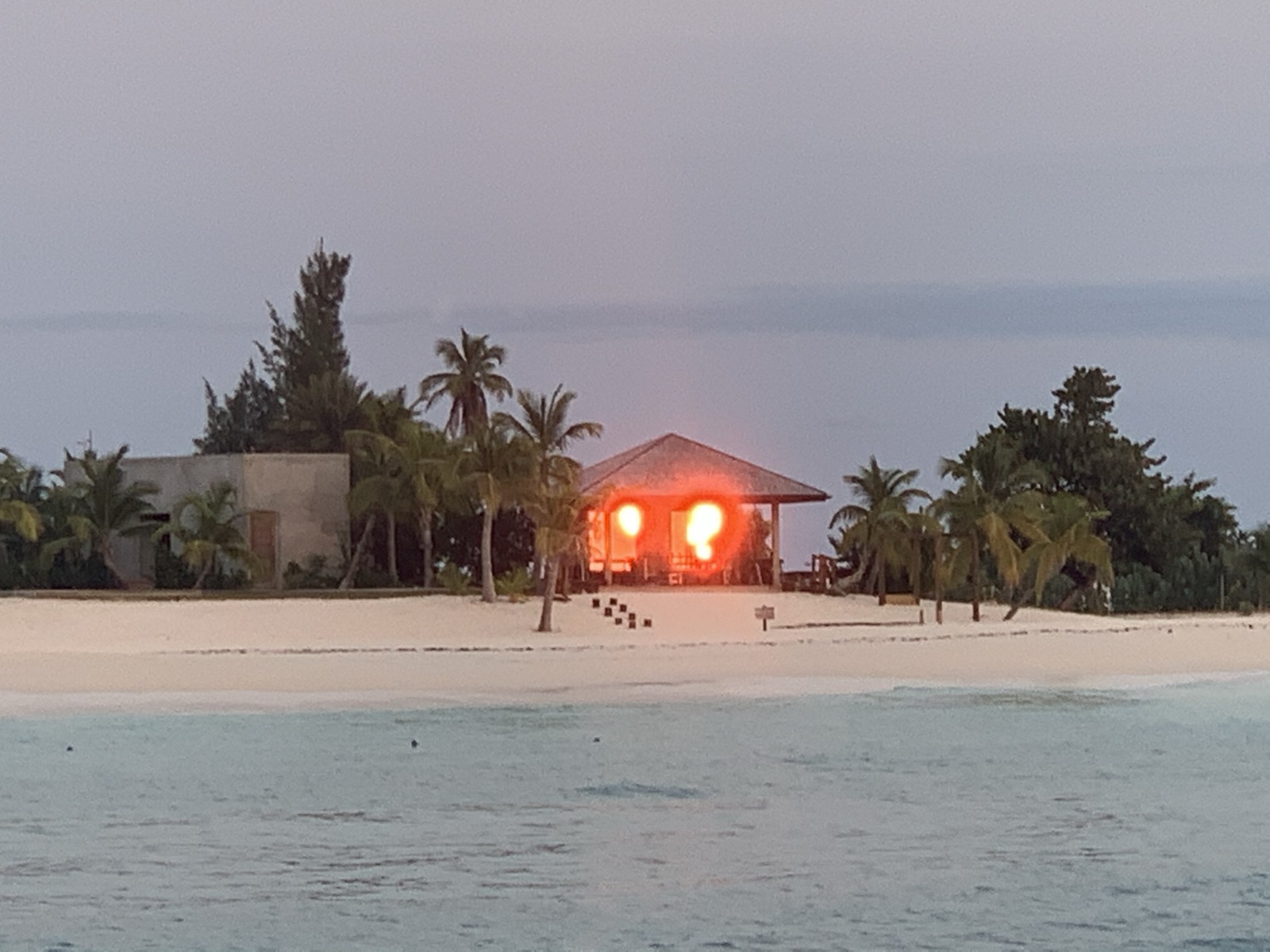 A small beach structure lit from inside at dusk — Barbuda at its most atmospheric