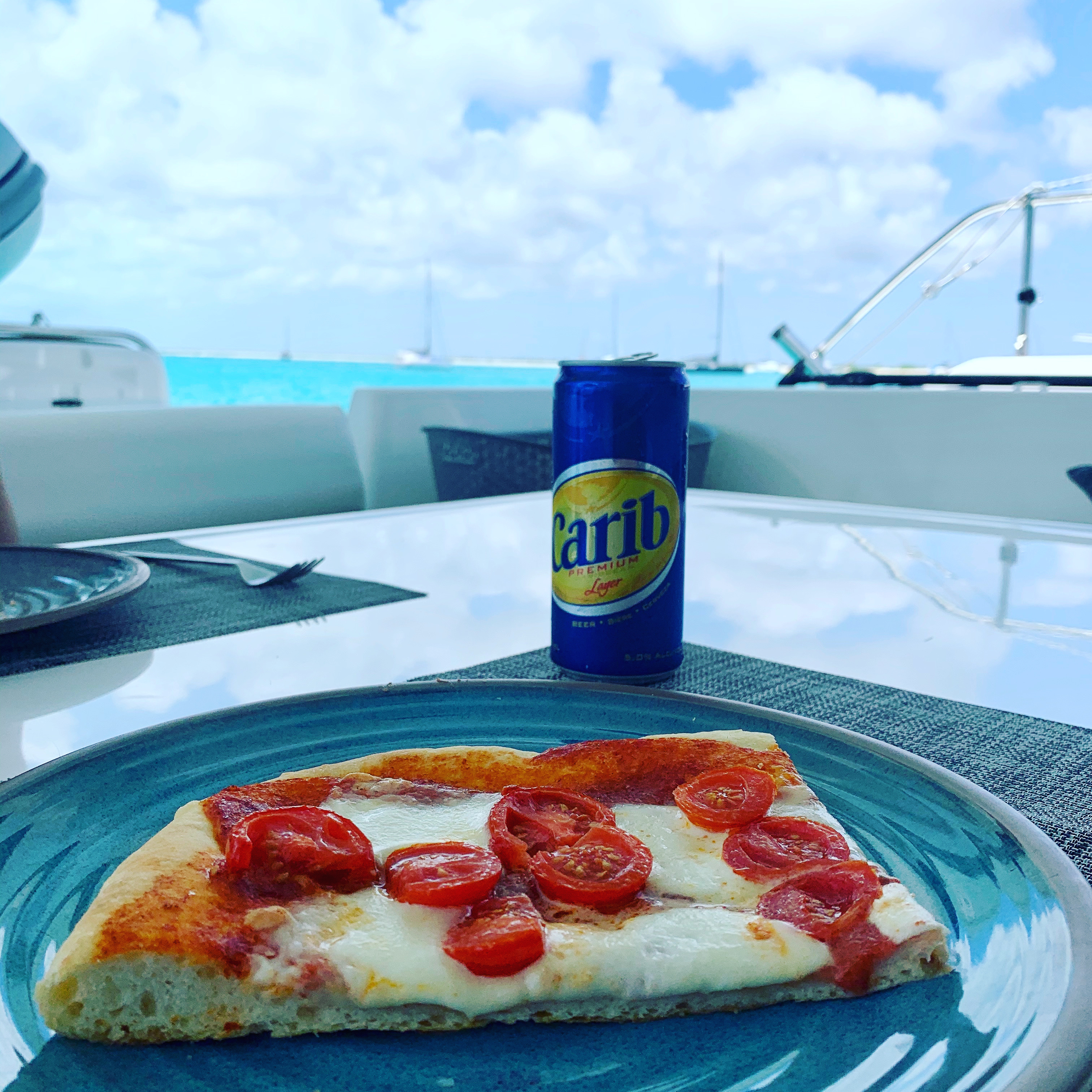 Pizza and a cold Carib on Oroboro's cockpit — boats in turquoise water behind