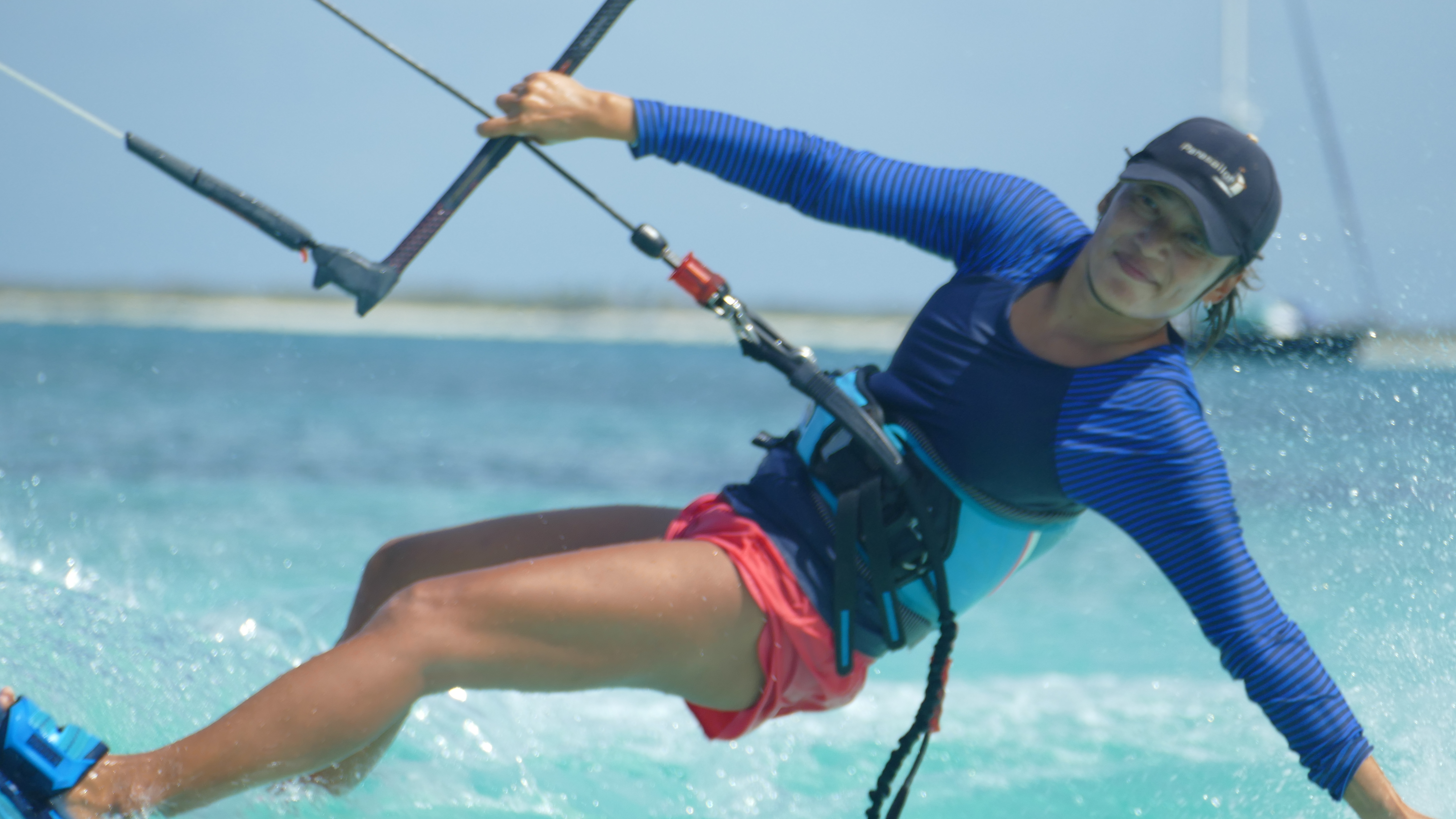 Yuka kiteboarding in Barbuda's turquoise water — big smile, blue rashguard