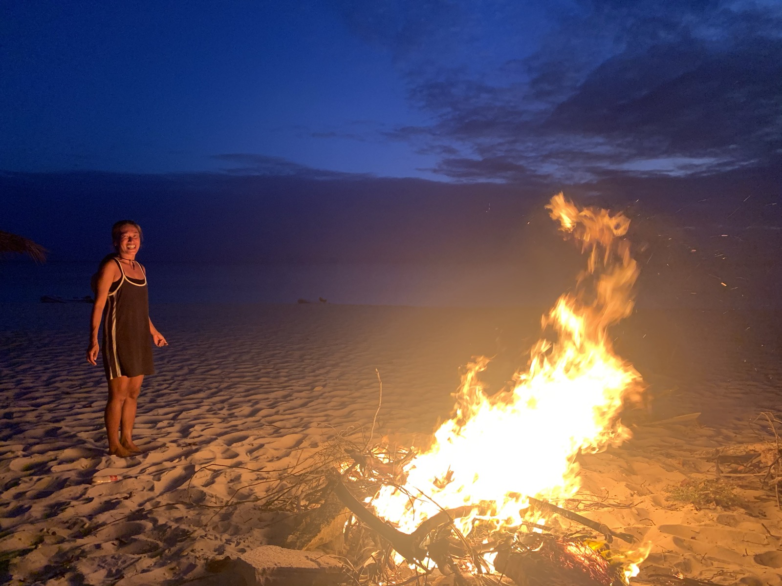 Yuka by a beach bonfire at night — Barbuda's deep blue dusk sky