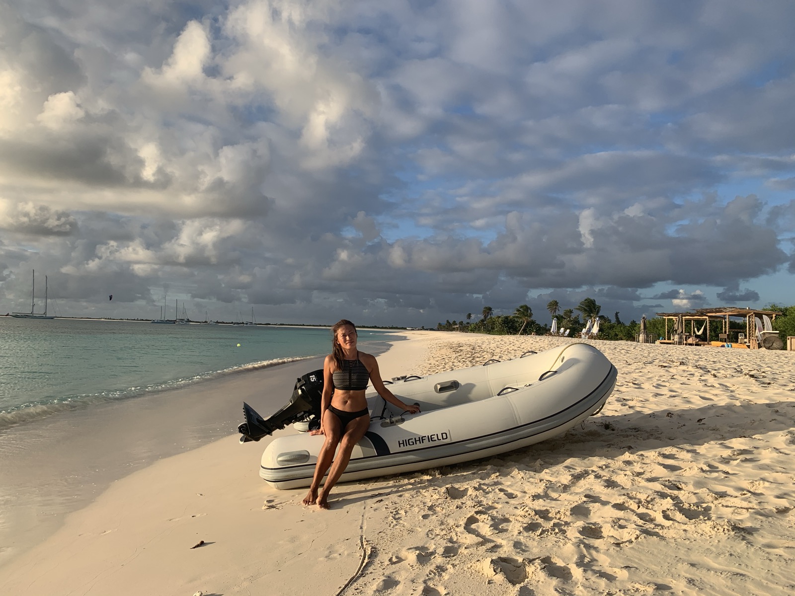 Yuka sitting on the Highfield dinghy on white sand, the anchorage behind her in golden hour light