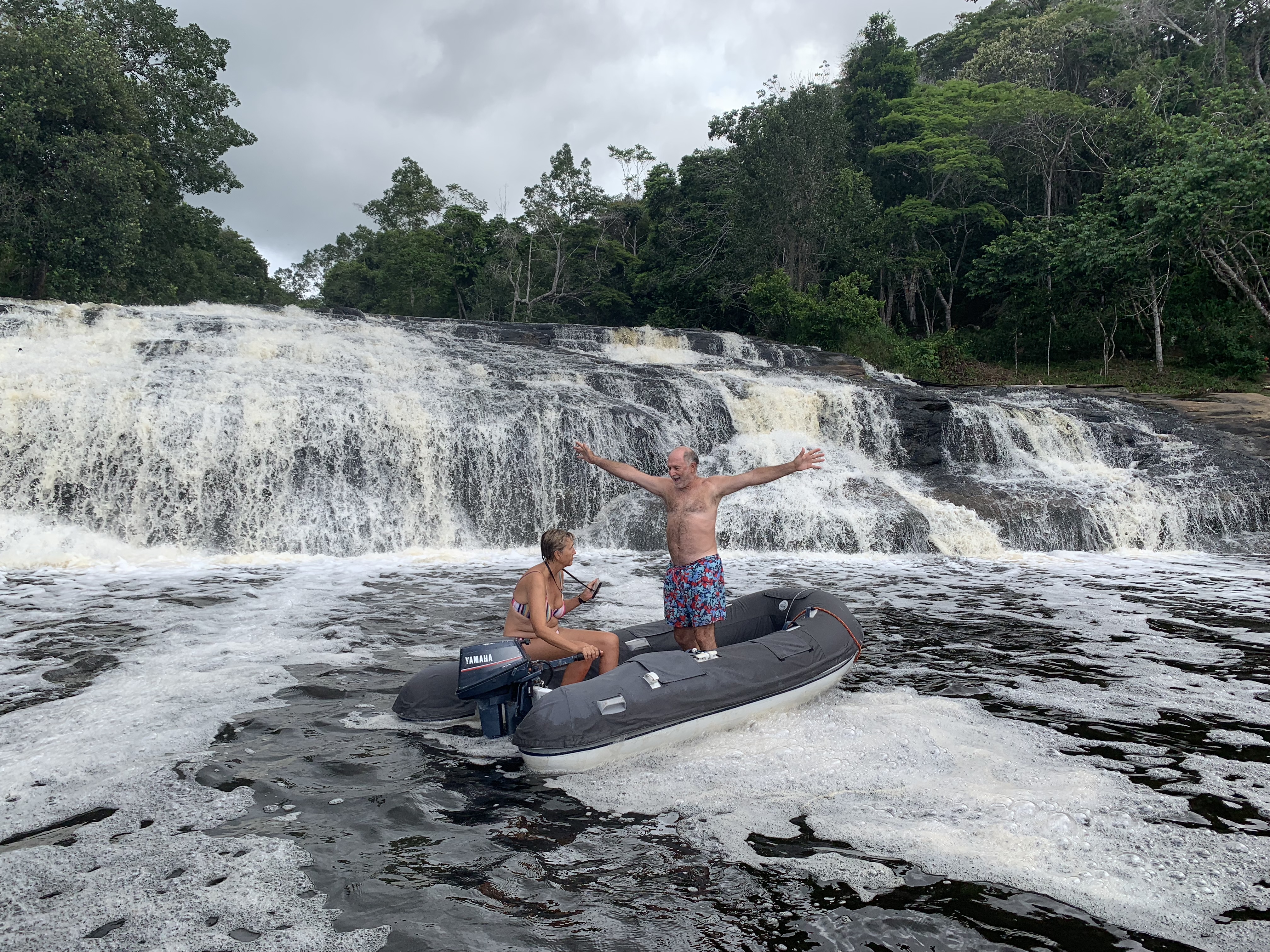 Francesco standing on the dinghy with arms spread wide in front of the waterfall