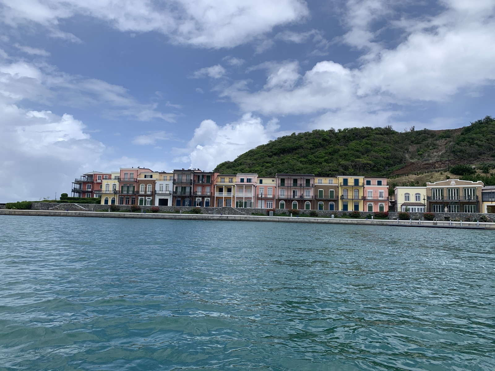 The Canouan marina waterfront seen from the water — a row of colourful colonial villas stretching across the hillside
