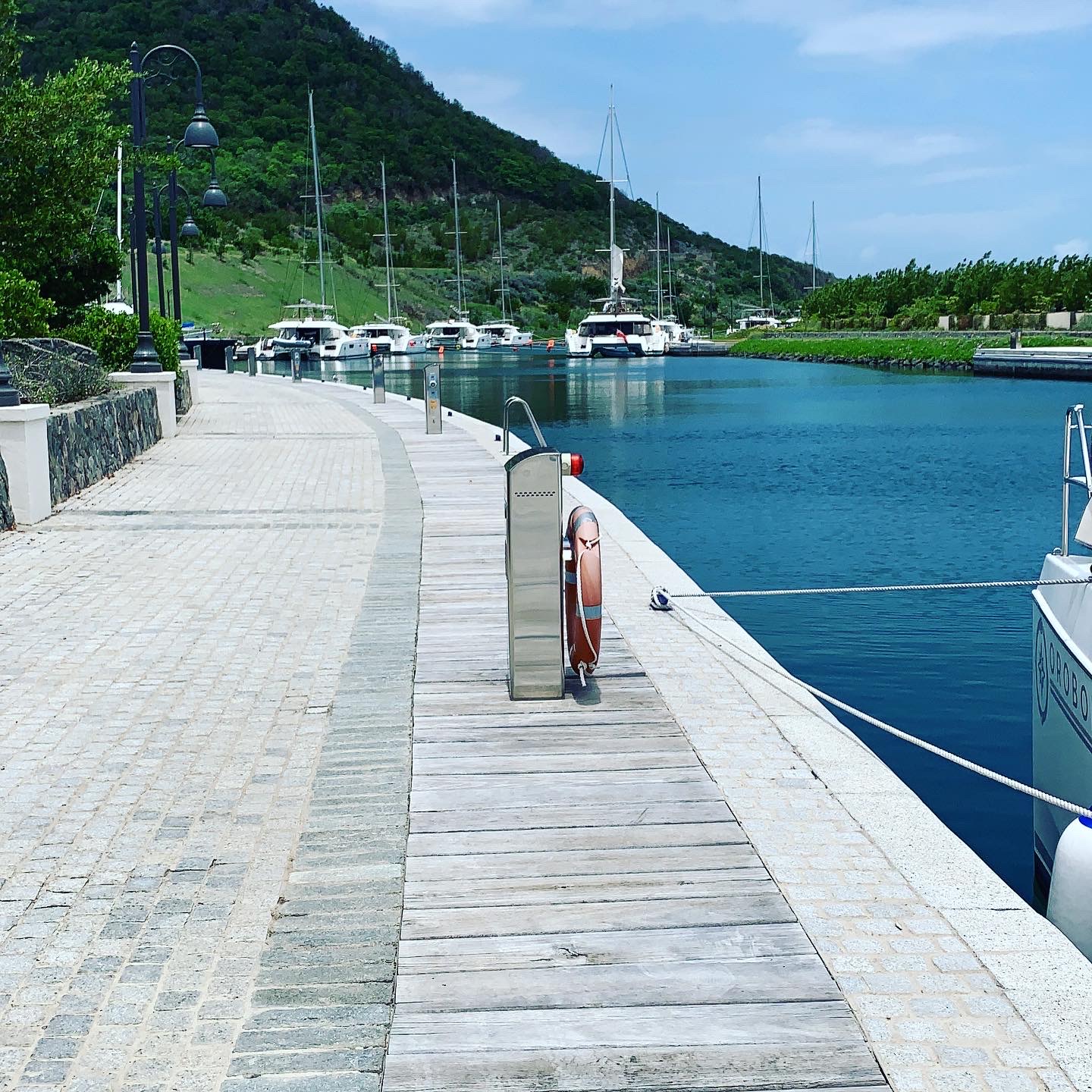 The Canouan marina promenade — cobblestone walkway, ornate gas lamp posts, and the protected lagoon beyond