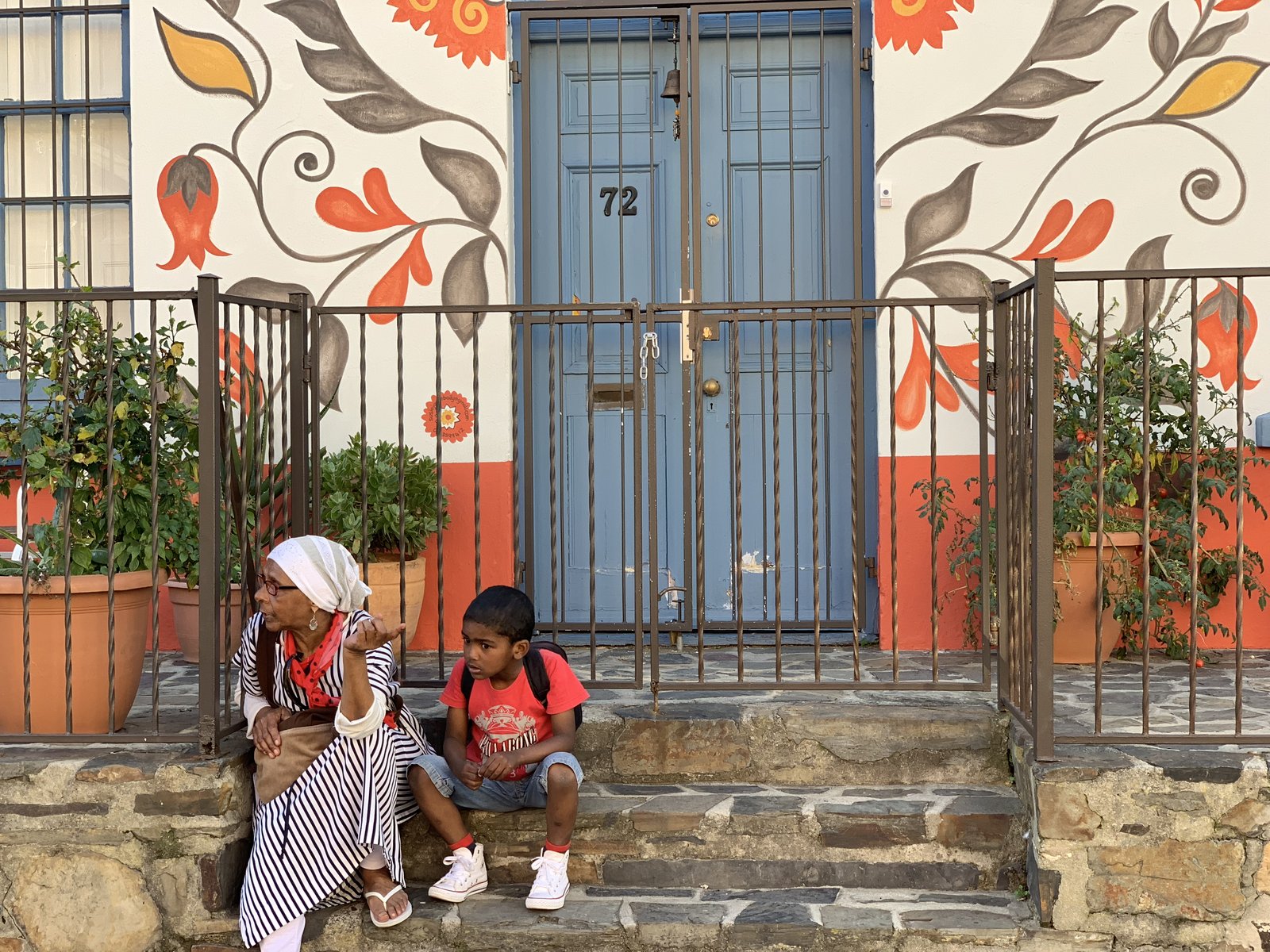 A woman and child sit on the steps of a painted doorway in Bo-Kaap