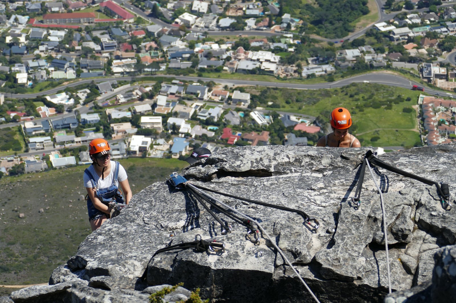 Rock climbers ascending a face on Table Mountain, Cape Town suburbs spread below