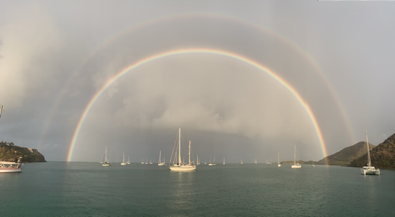 A full double rainbow arching over an anchorage crowded with sailboats