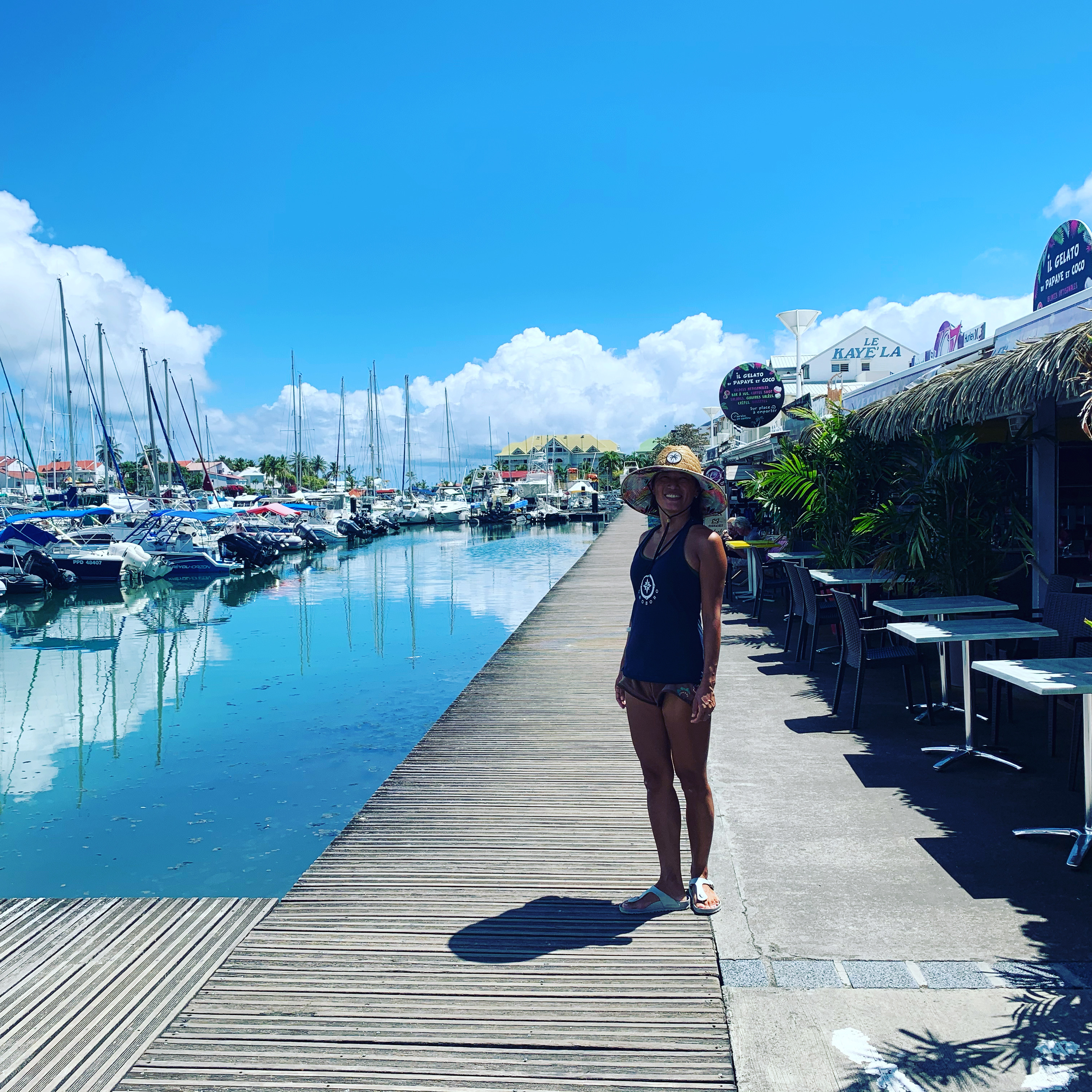 Yuka on the marina boardwalk in Guadeloupe — sailboats reflected in flat water, Le Kaye La restaurant behind her