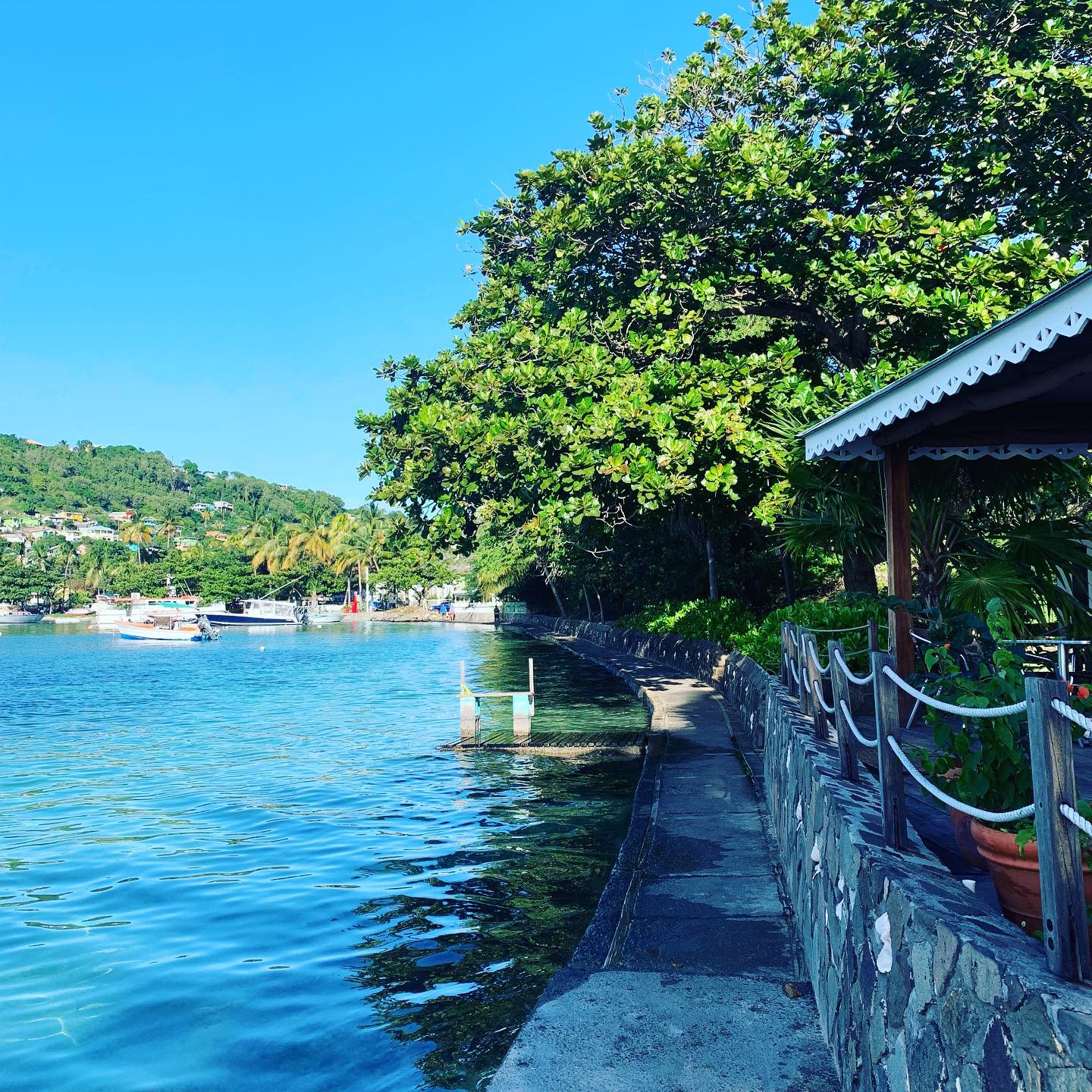 A calm Caribbean bay with a stone seawall and boats moored alongside