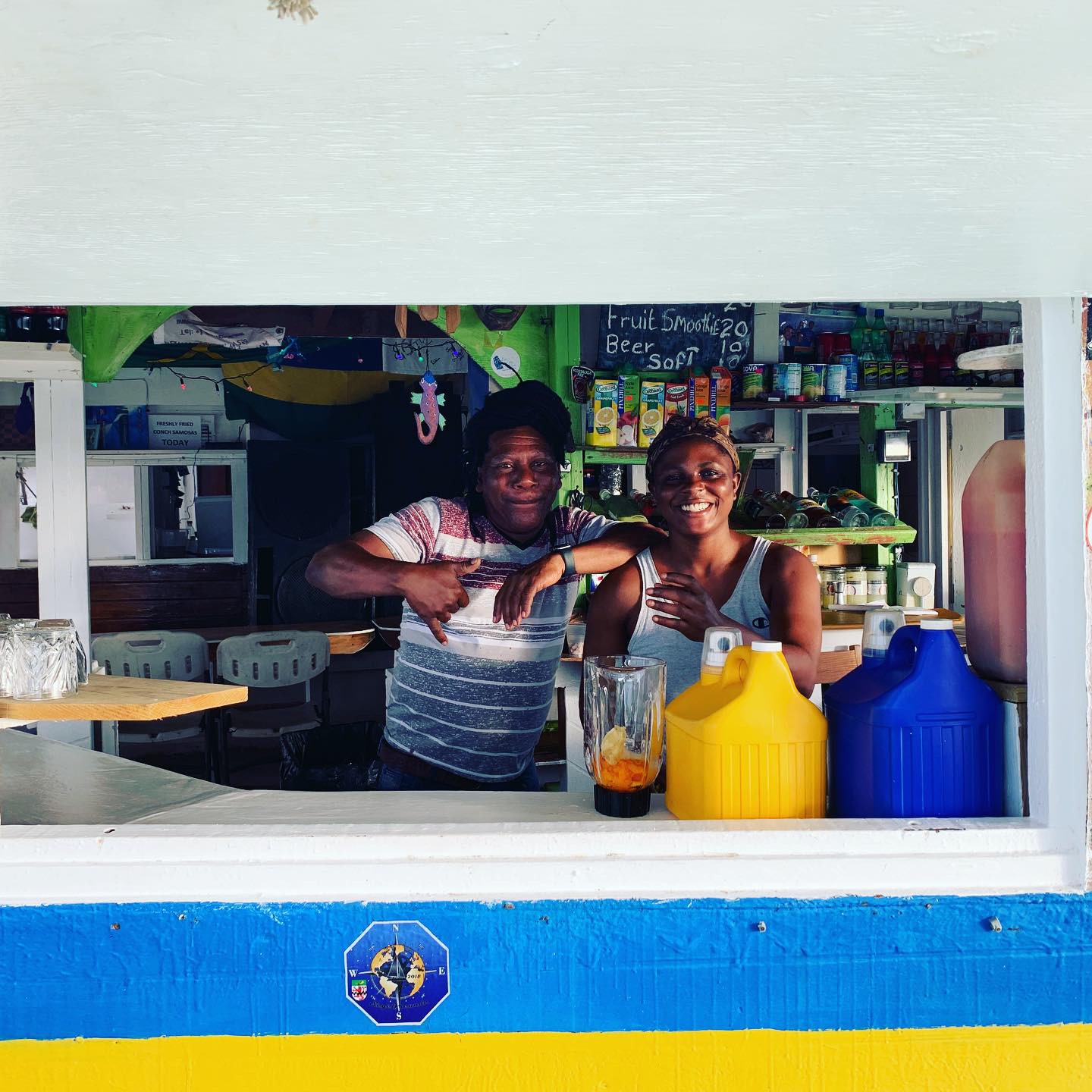 Two locals smiling from behind a colorful Caribbean bar counter