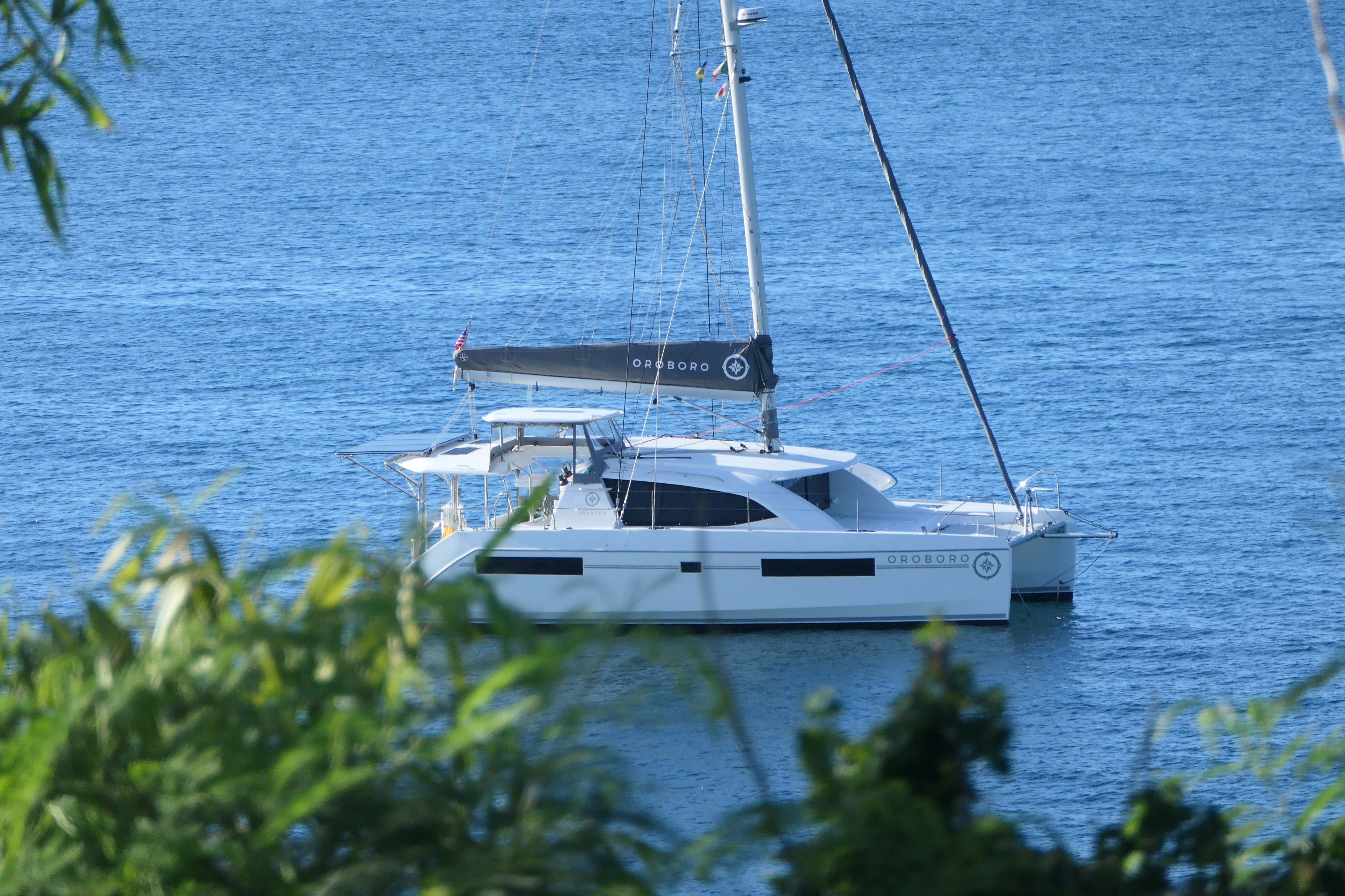 Oroboro at anchor in a sheltered bay, framed by tropical foliage