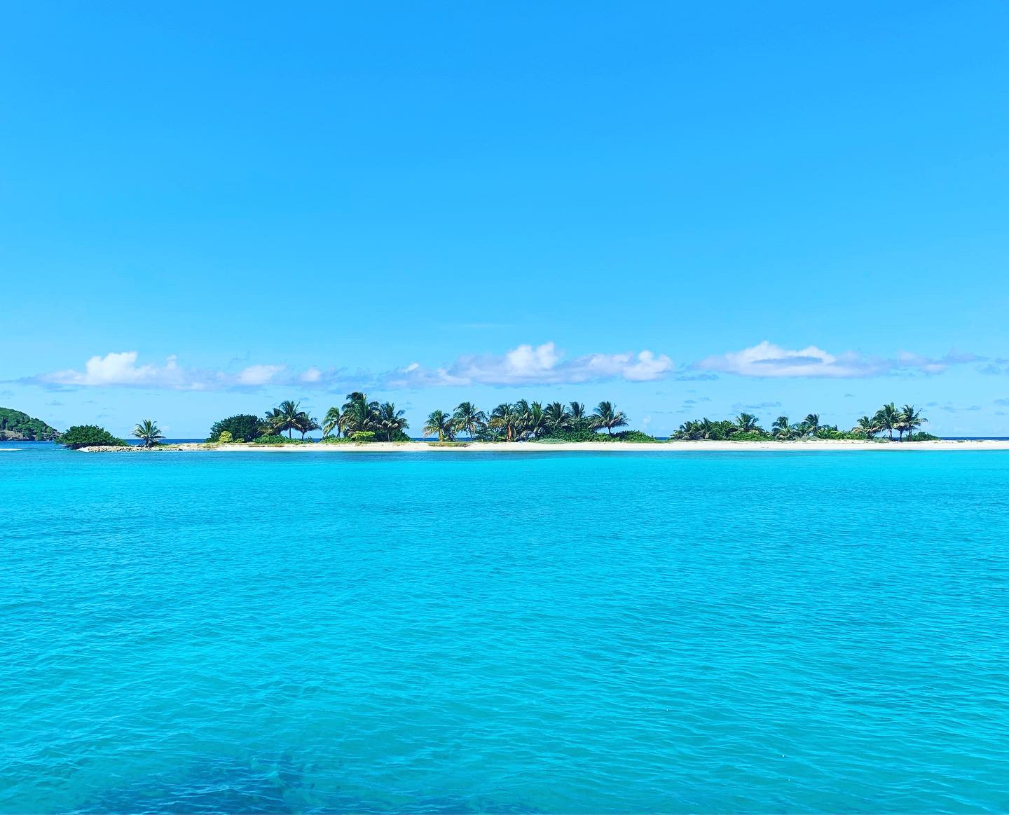 A small palm-fringed sandbar island surrounded by brilliant turquoise water