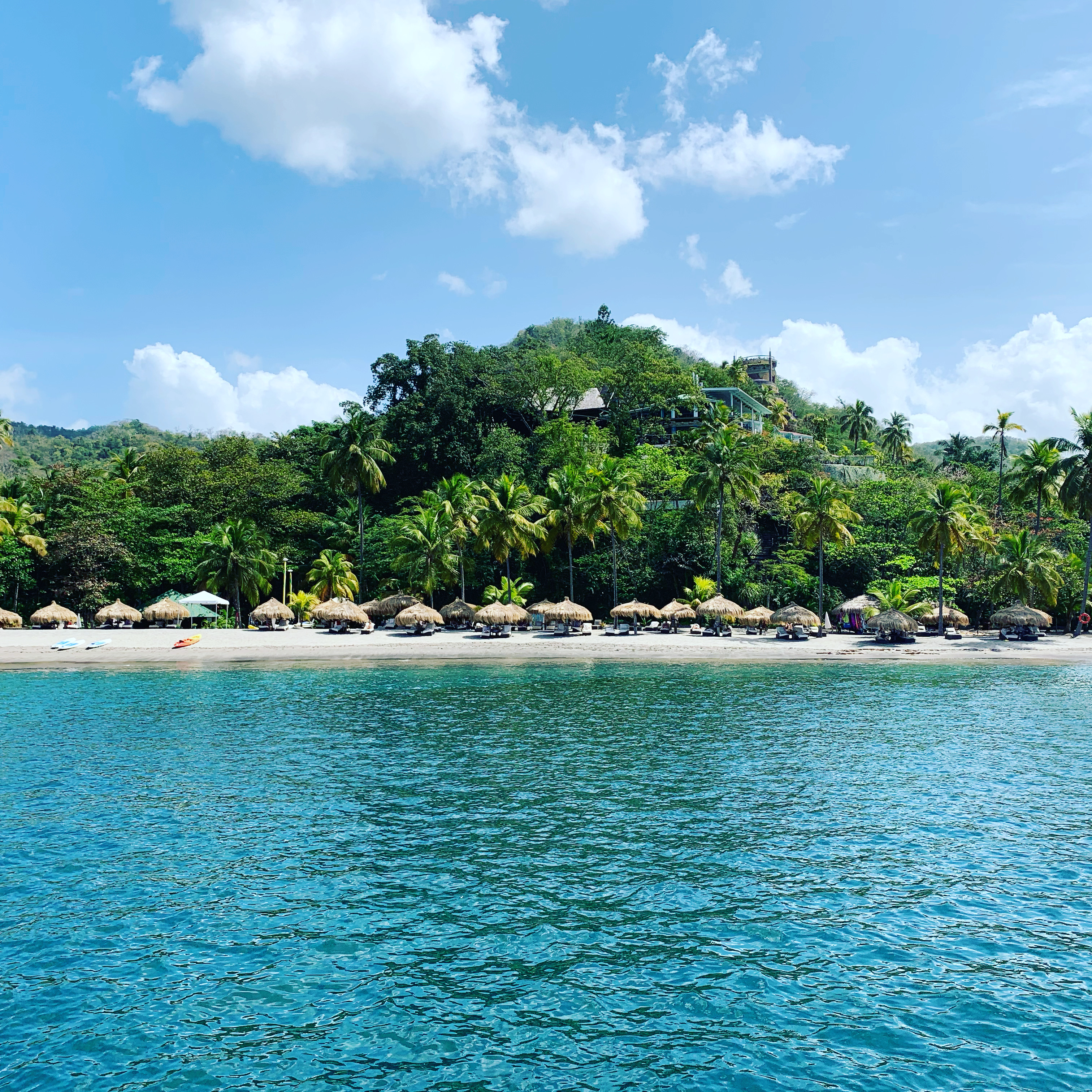 A tropical beach in St Lucia — thatched umbrellas, loungers, and a dense jungle hillside above