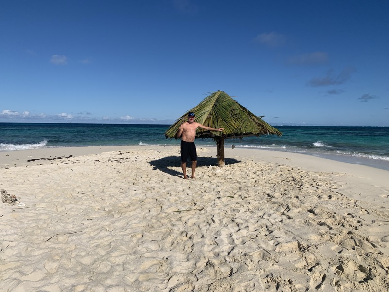 Francesco beside a lone palm-leaf thatched shelter on a windy white sand beach