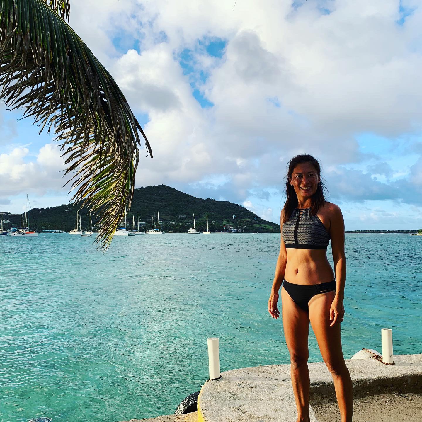 Yuka on a waterfront dock — the green harbor hills behind her
