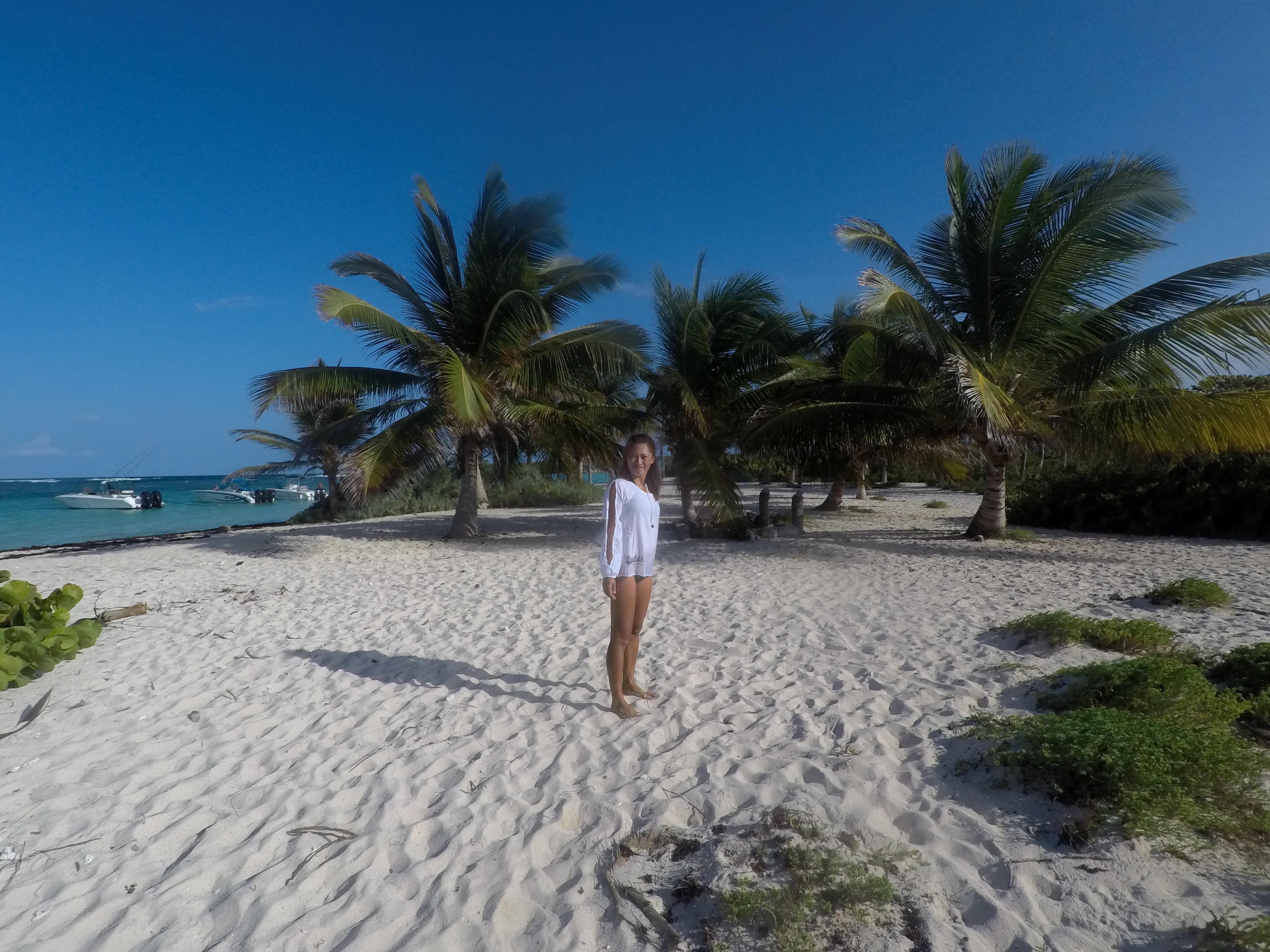 Yuka in a white dress on a white sand beach among palm trees
