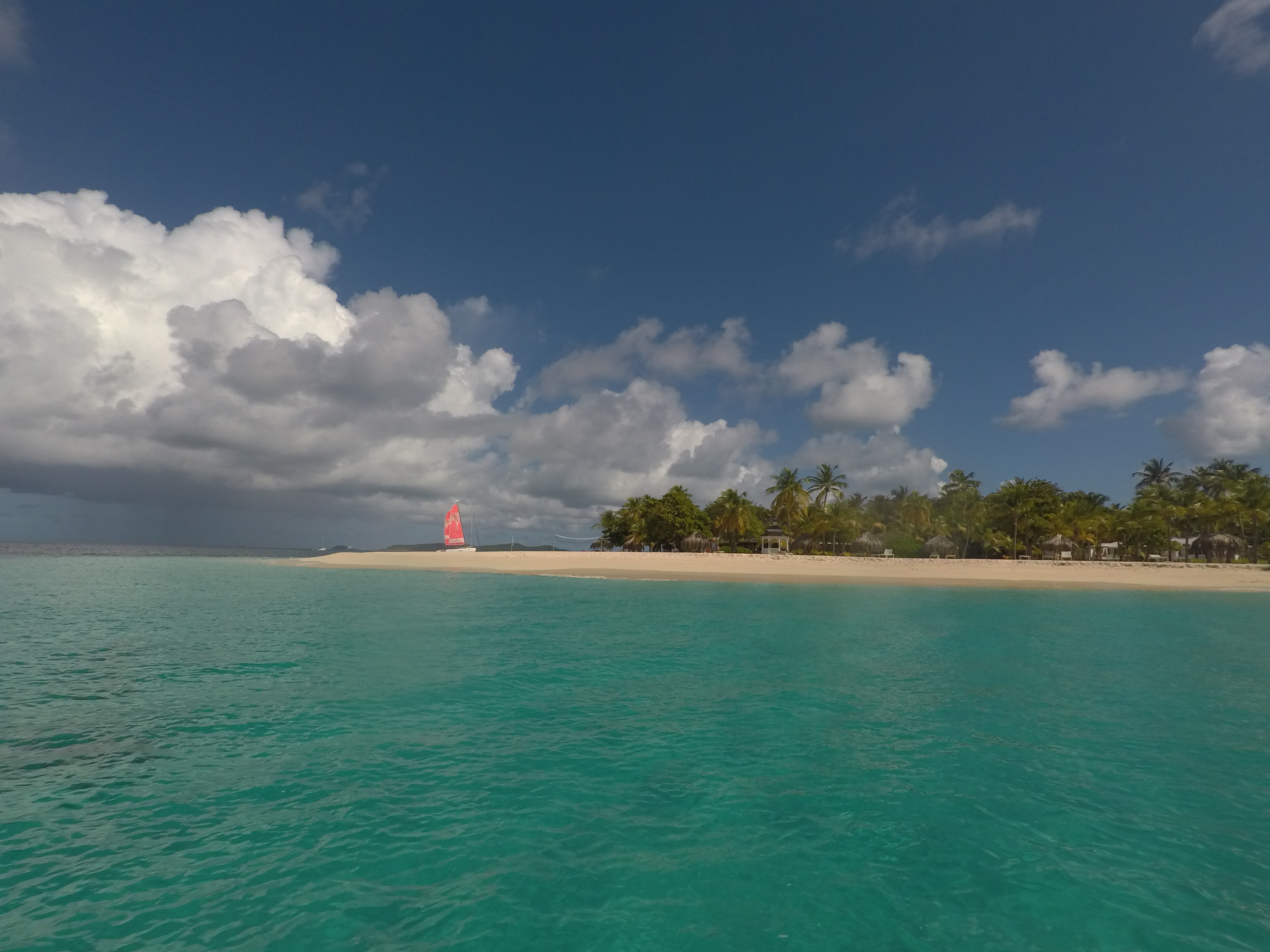 A perfect white sand Grenadines beach with a small red-sailed beach catamaran at the waterline