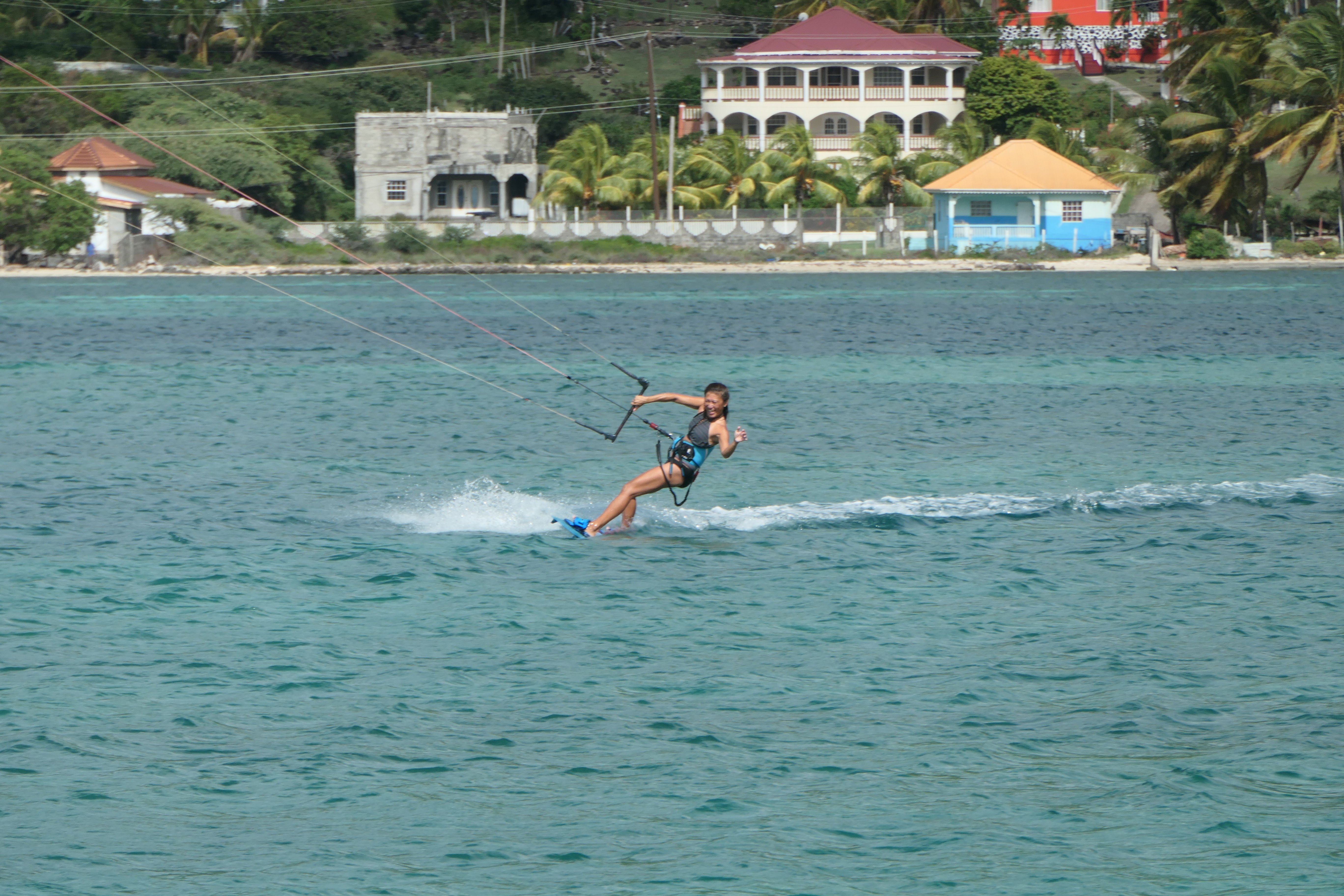 Yuka kiteboarding with the village and coastline visible on shore behind her