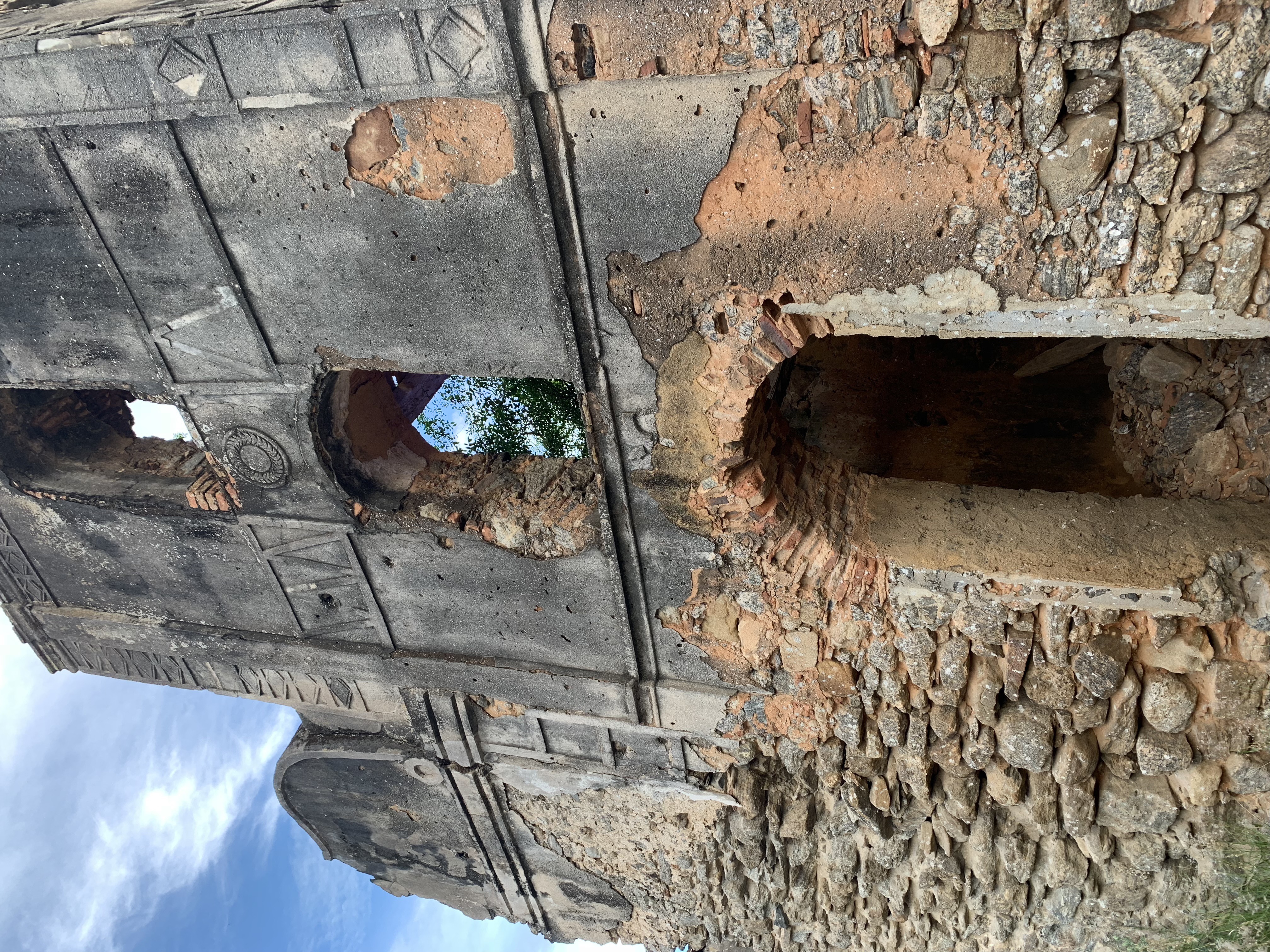 Ruínas de um edifício da época colonial ao lado da igreja — arcos de pedra expostos e paredes de tijolos em ruínas lentamente retomadas pelo tempo