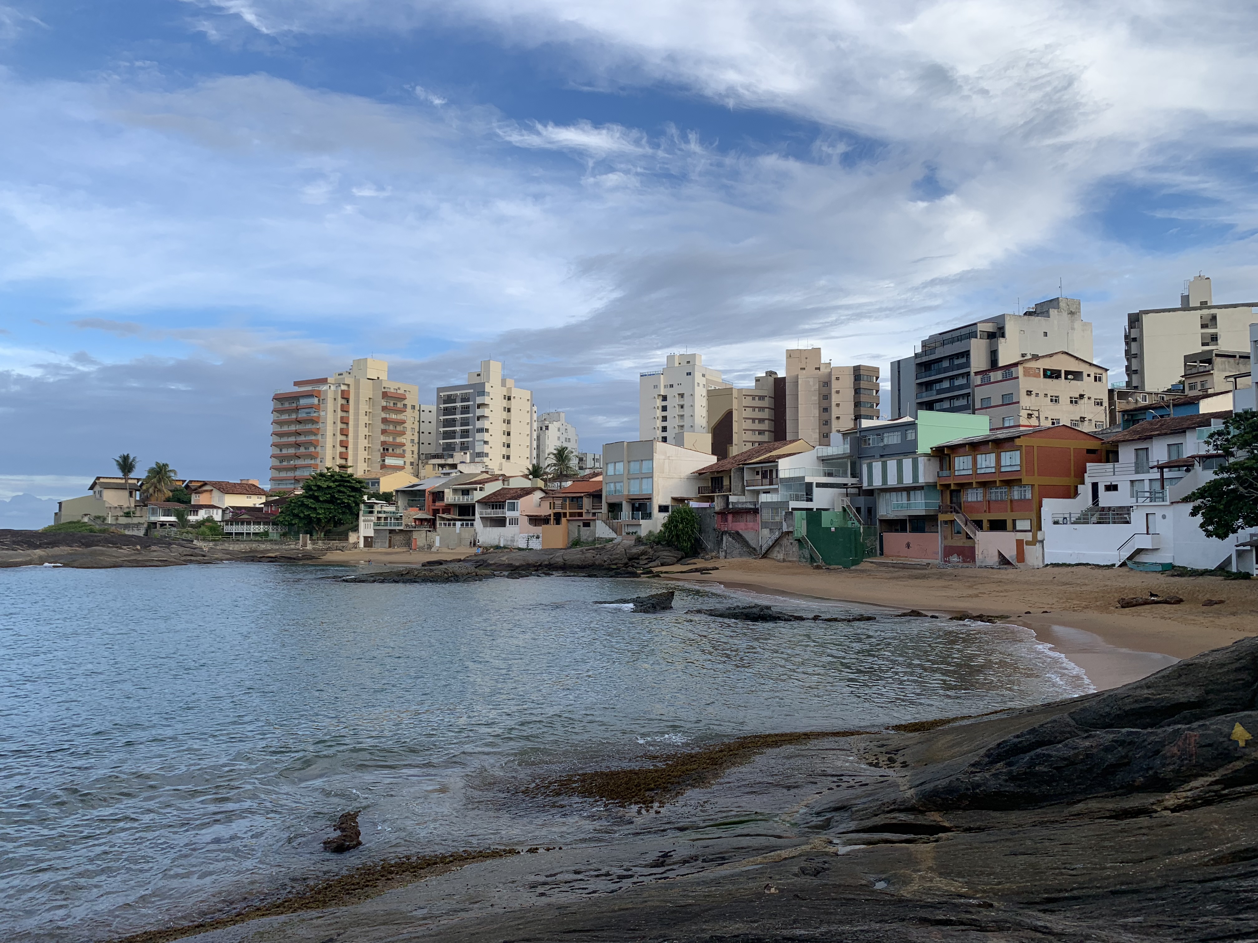 Orla urbana de Guarapari — prédios de apartamentos se erguem atrás de um litoral rochoso típico da costa do Espírito Santo