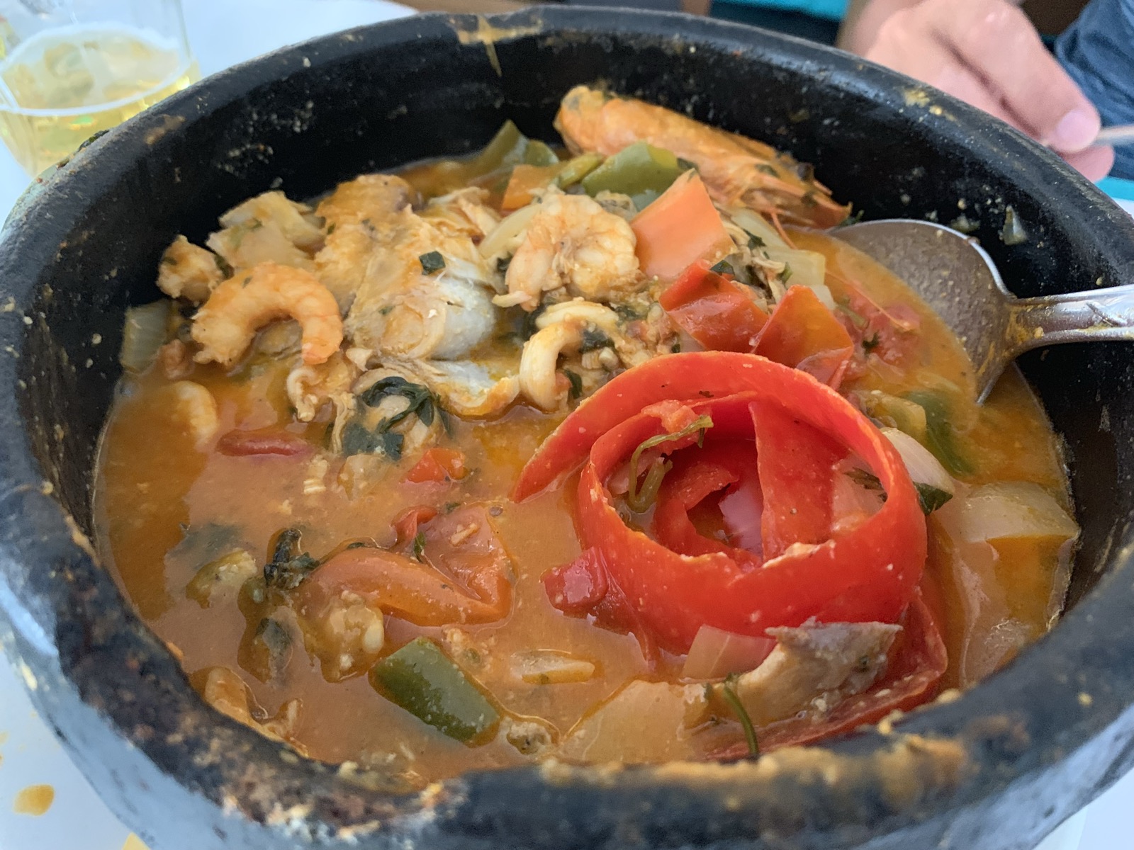 Moqueca de frutos do mar numa panela de barro com camarão, peixe, pimentão vermelho e tomates num caldo alaranjado e encorpado