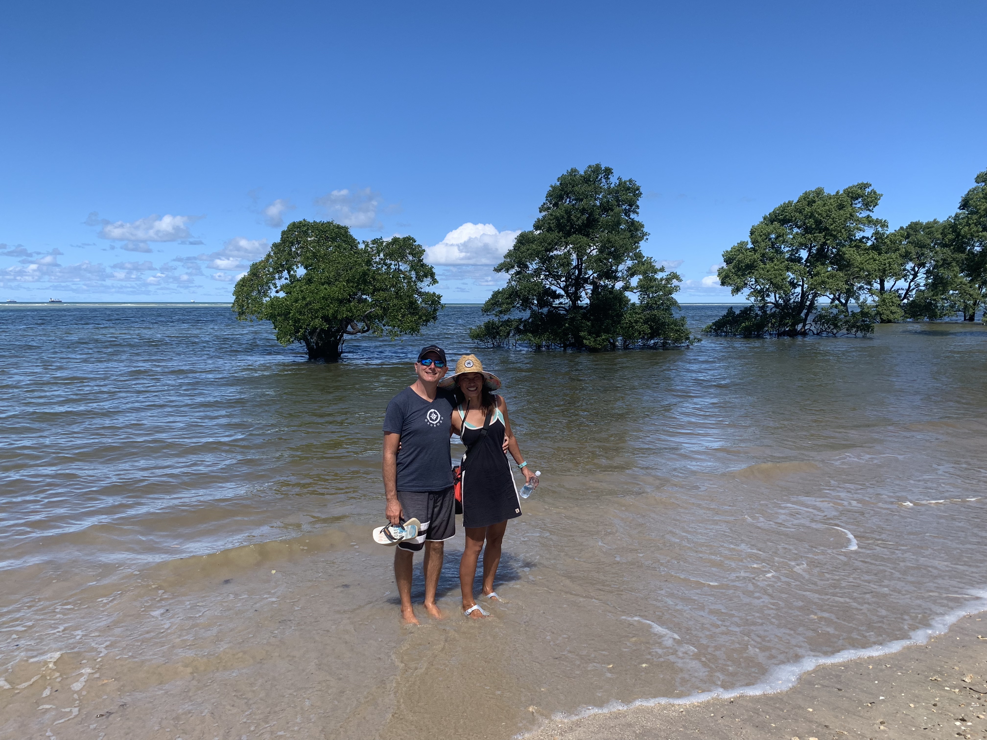 Francesco e Yuka parados nas planícies de maré rasas de Jiribatuba, com árvores de mangue emergindo da água ao redor deles