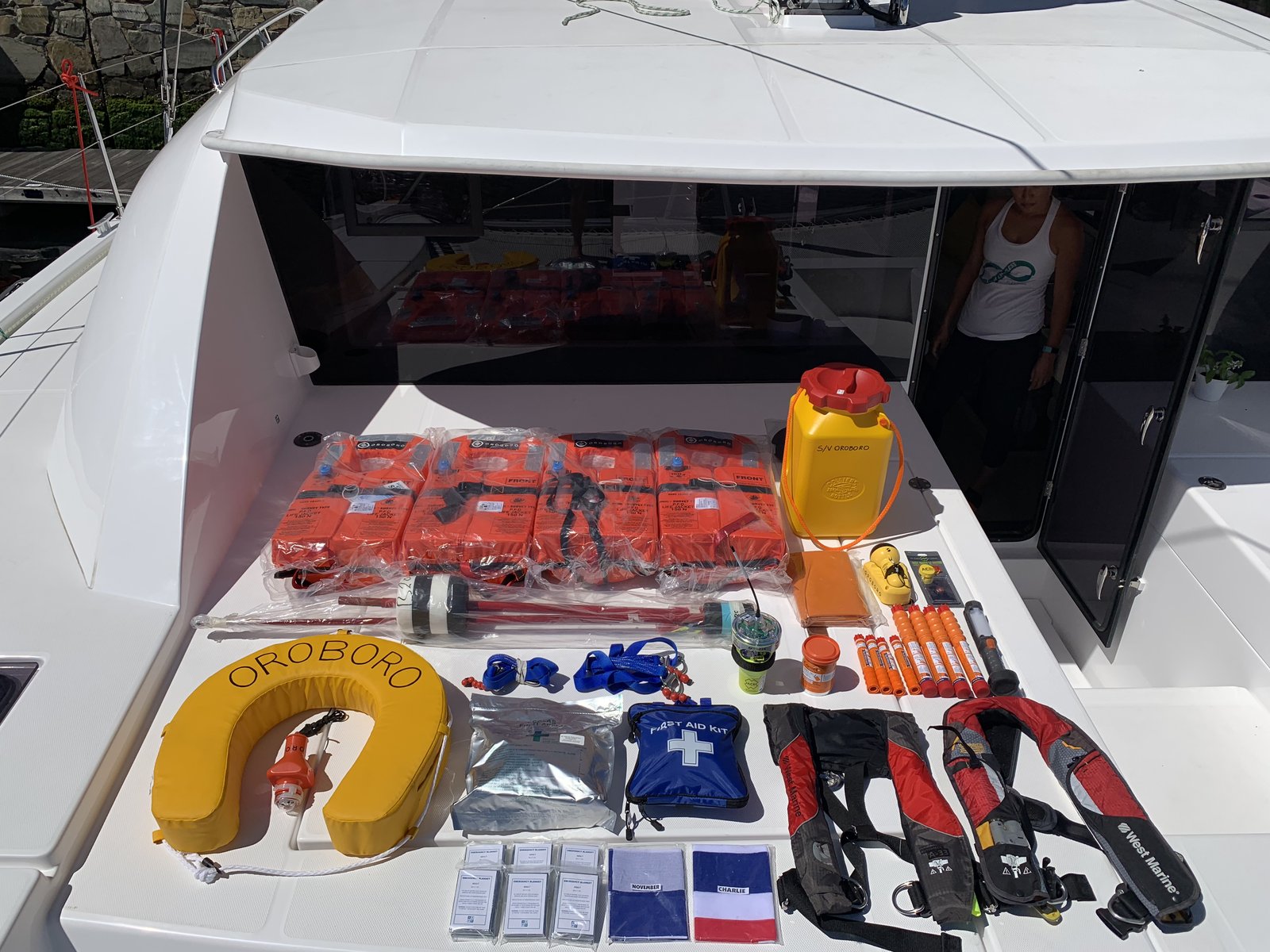 Full safety equipment inventory spread on the foredeck — life jackets, EPIRB, flares, tethers, PLBs, and the Oroboro life ring