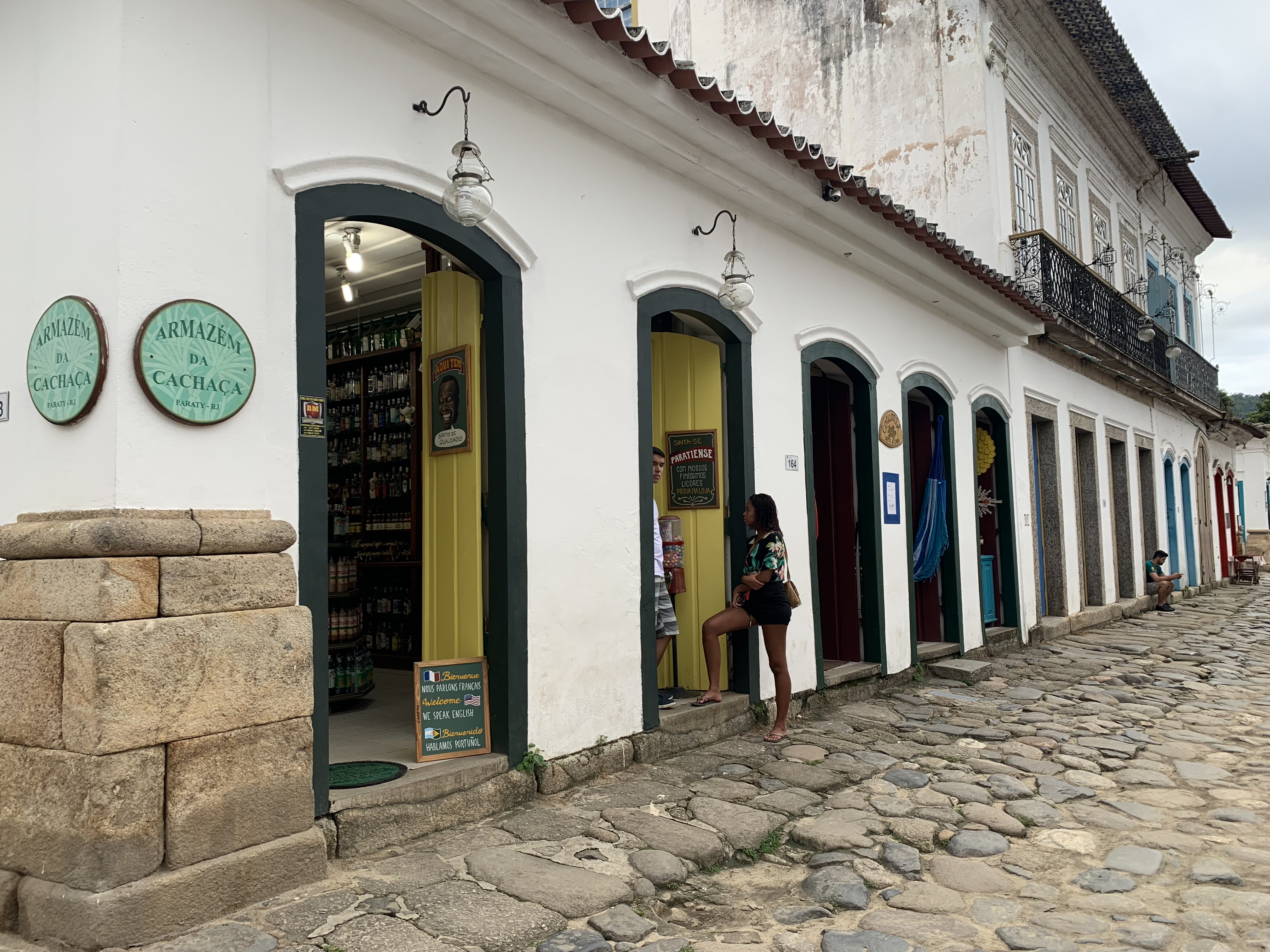Fachada da loja Armazém da Cachaça em uma rua colonial de Paraty, paredes caiadas de branco com o nome exibido acima da porta
