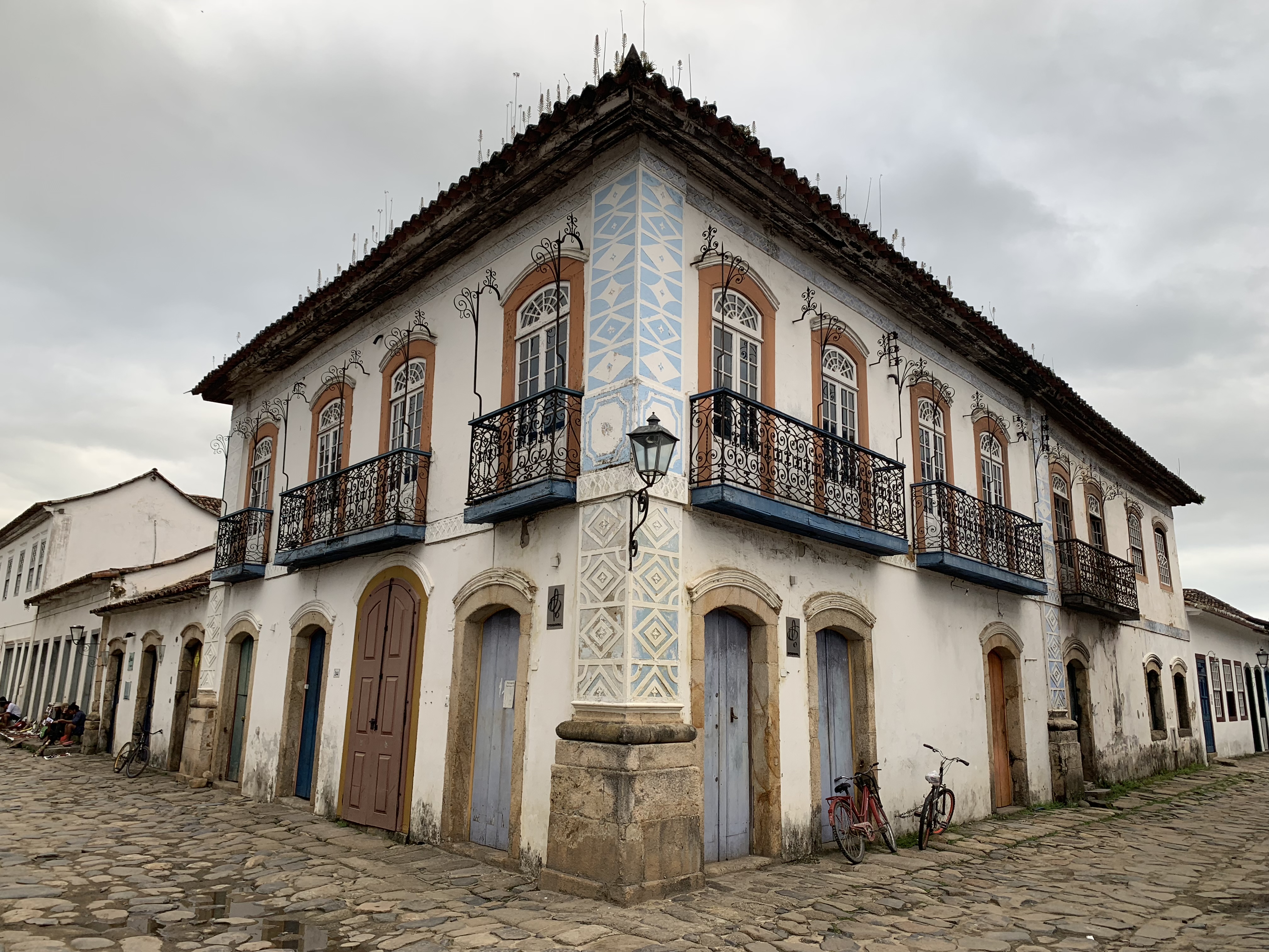 Imponente edifício colonial de esquina em dois andares em Paraty, com padrões decorativos geométricos na fachada, janelas e portas em arco pintadas de azul profundo e varanda de ferro forjado