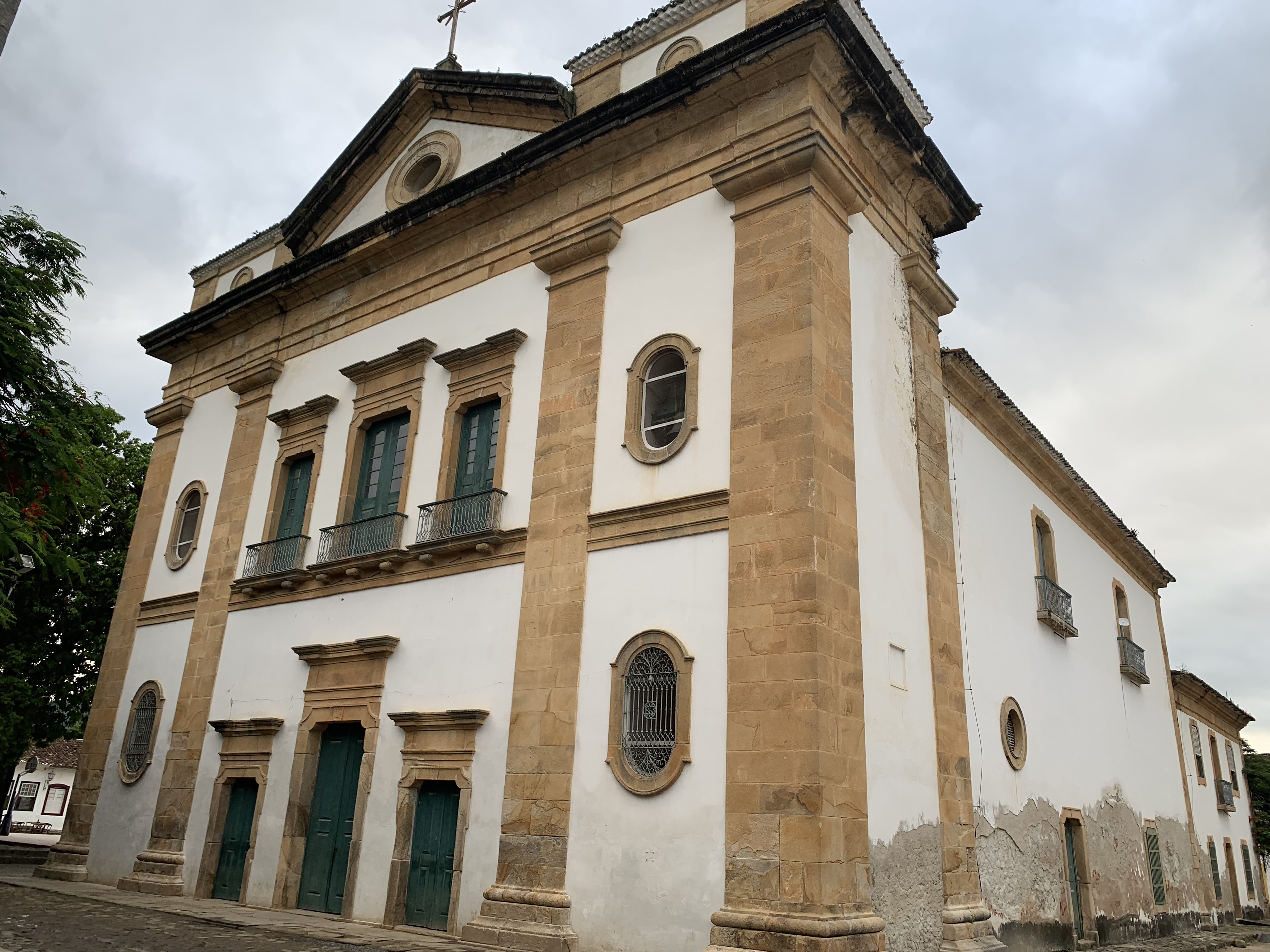 A fachada barroca de uma grande igreja colonial de pedra em Paraty com torre sineira, recortada contra um céu parcialmente nublado