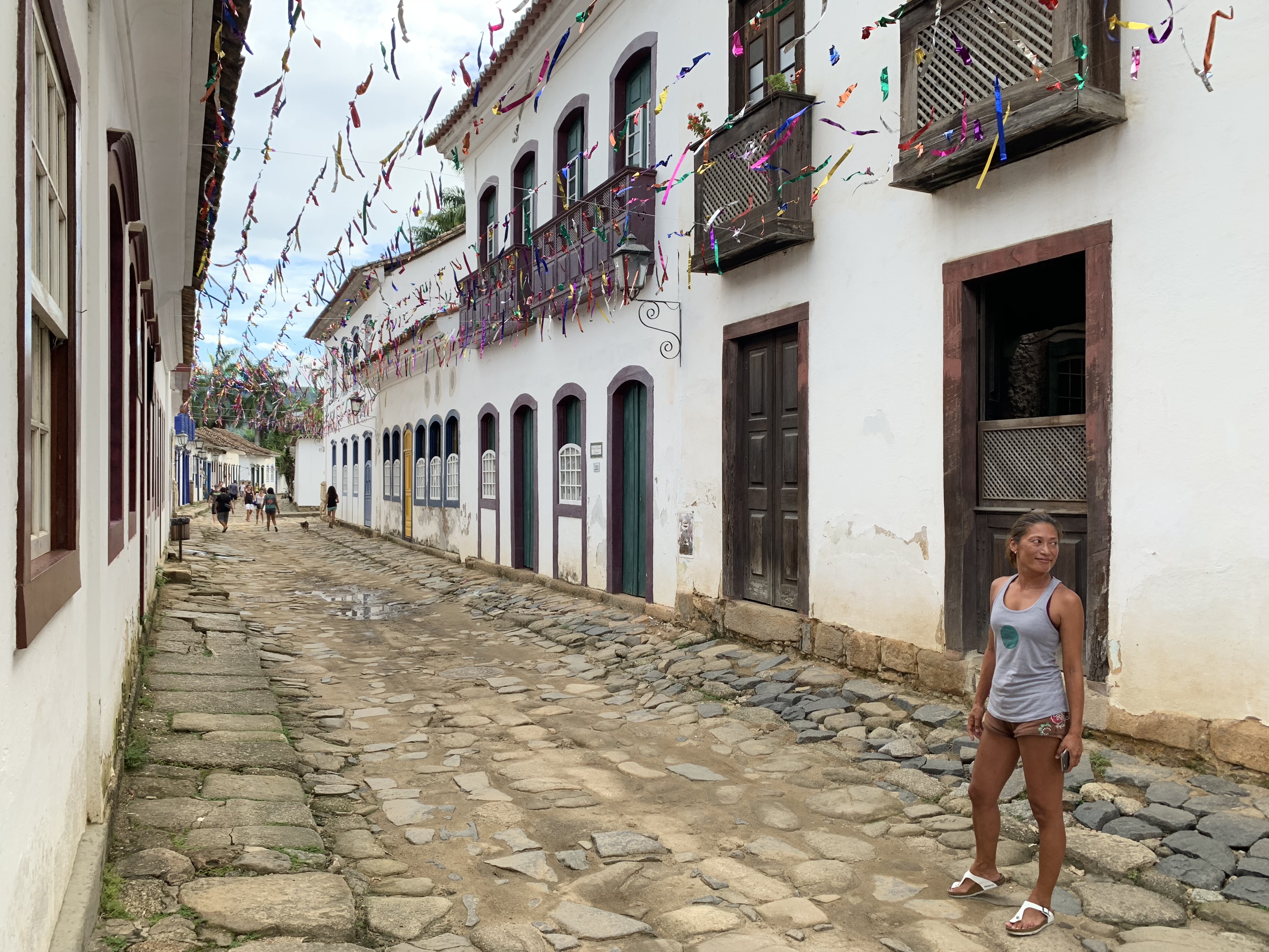 Yuka em uma rua de paralelepípedos de Paraty enfeitada com coloridas bandeirinhas de papel torcido entre os edifícios coloniais para um festival local