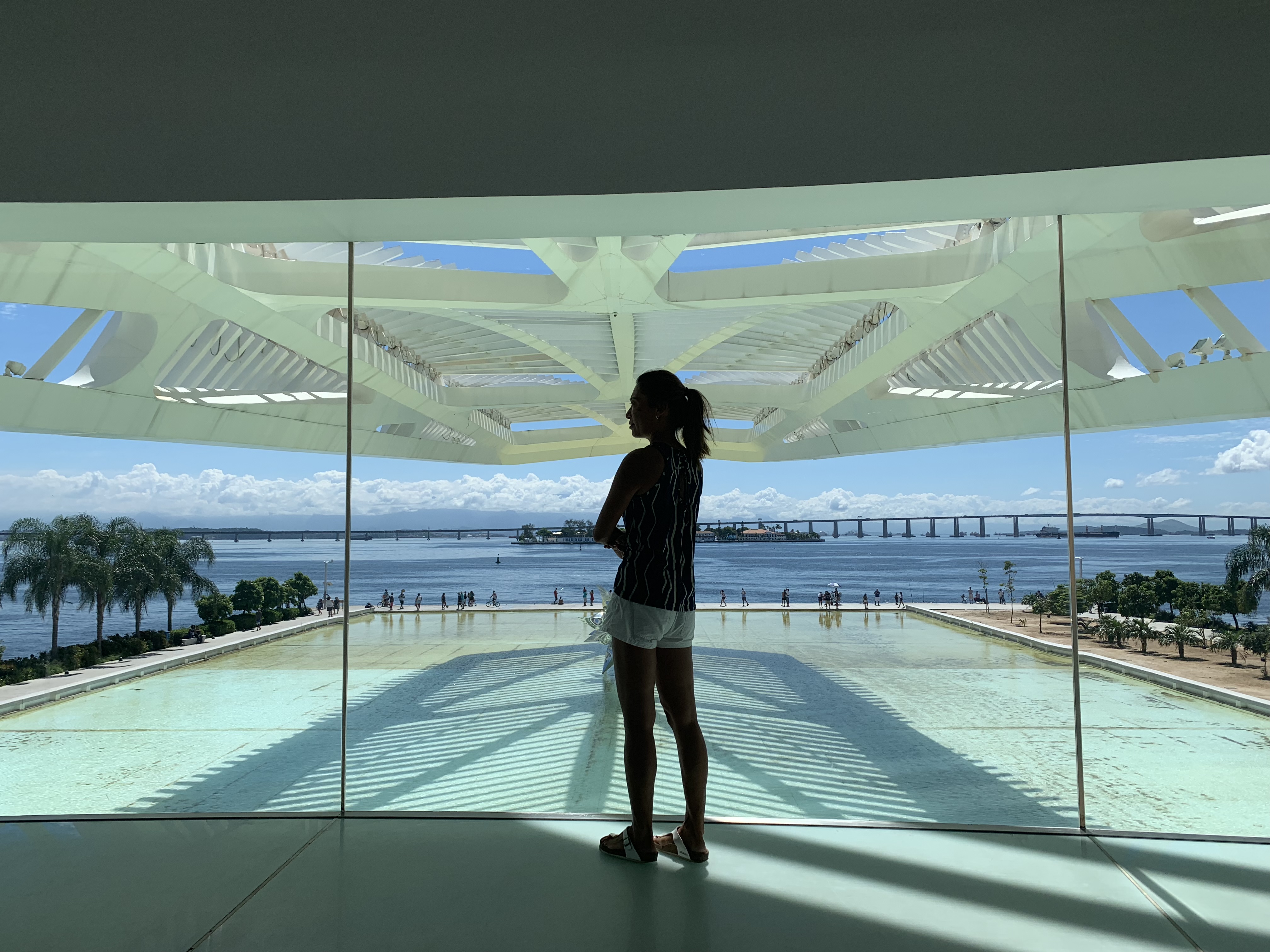 Yuka standing silhouetted at the glass wall of the Museu do Amanha overlooking Guanabara Bay