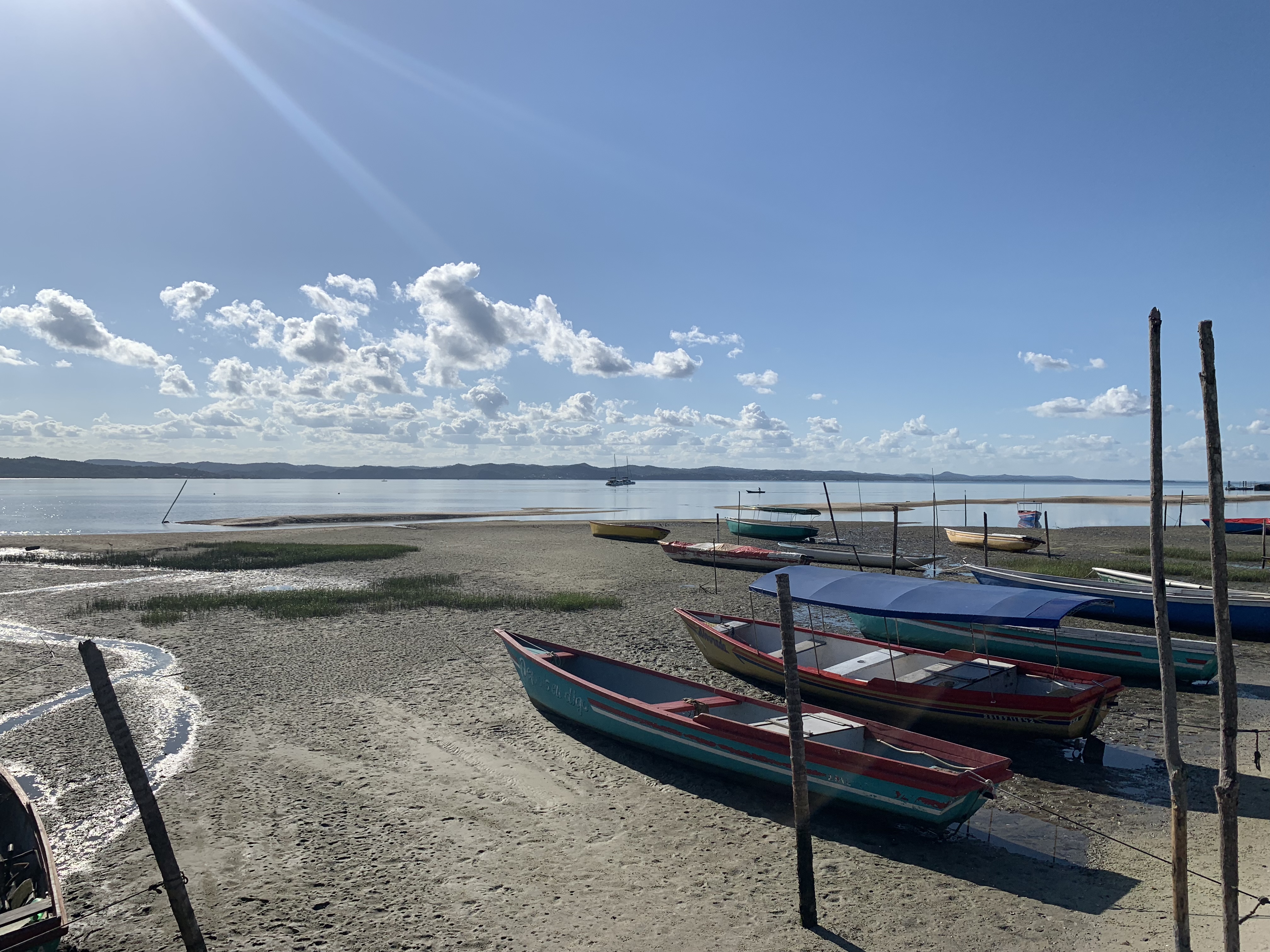 Coloridos barcos de pesca tradicionais de madeira puxados sobre a areia na maré baixa em Salinas da Margarida, com um catamarã fundeado ao fundo