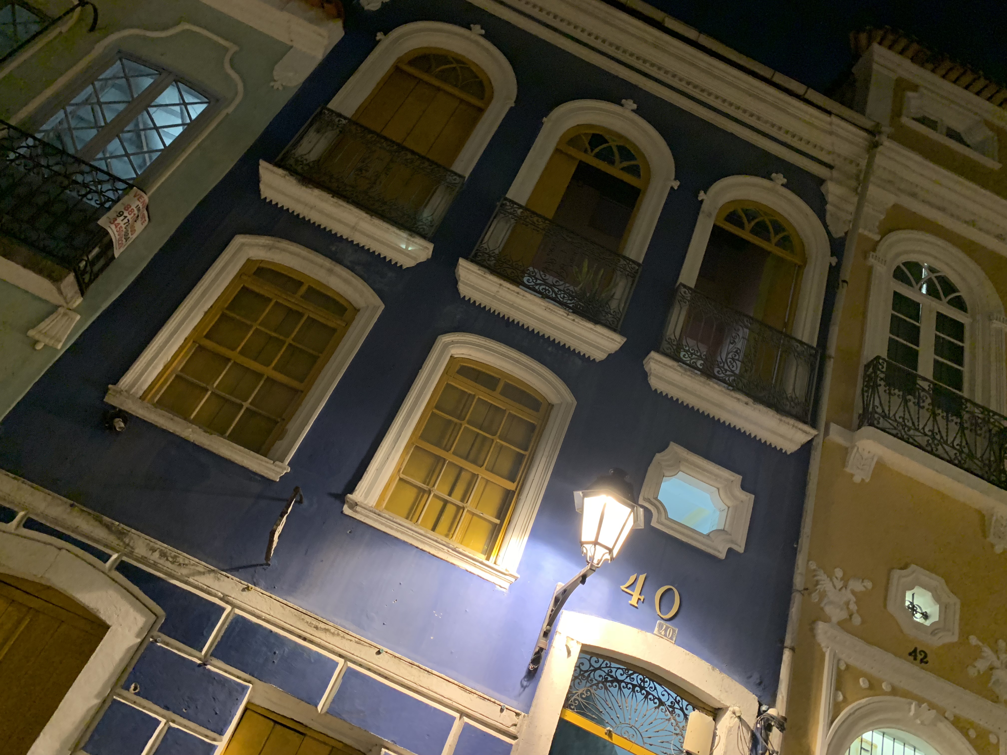 A blue colonial building at night with glowing windows