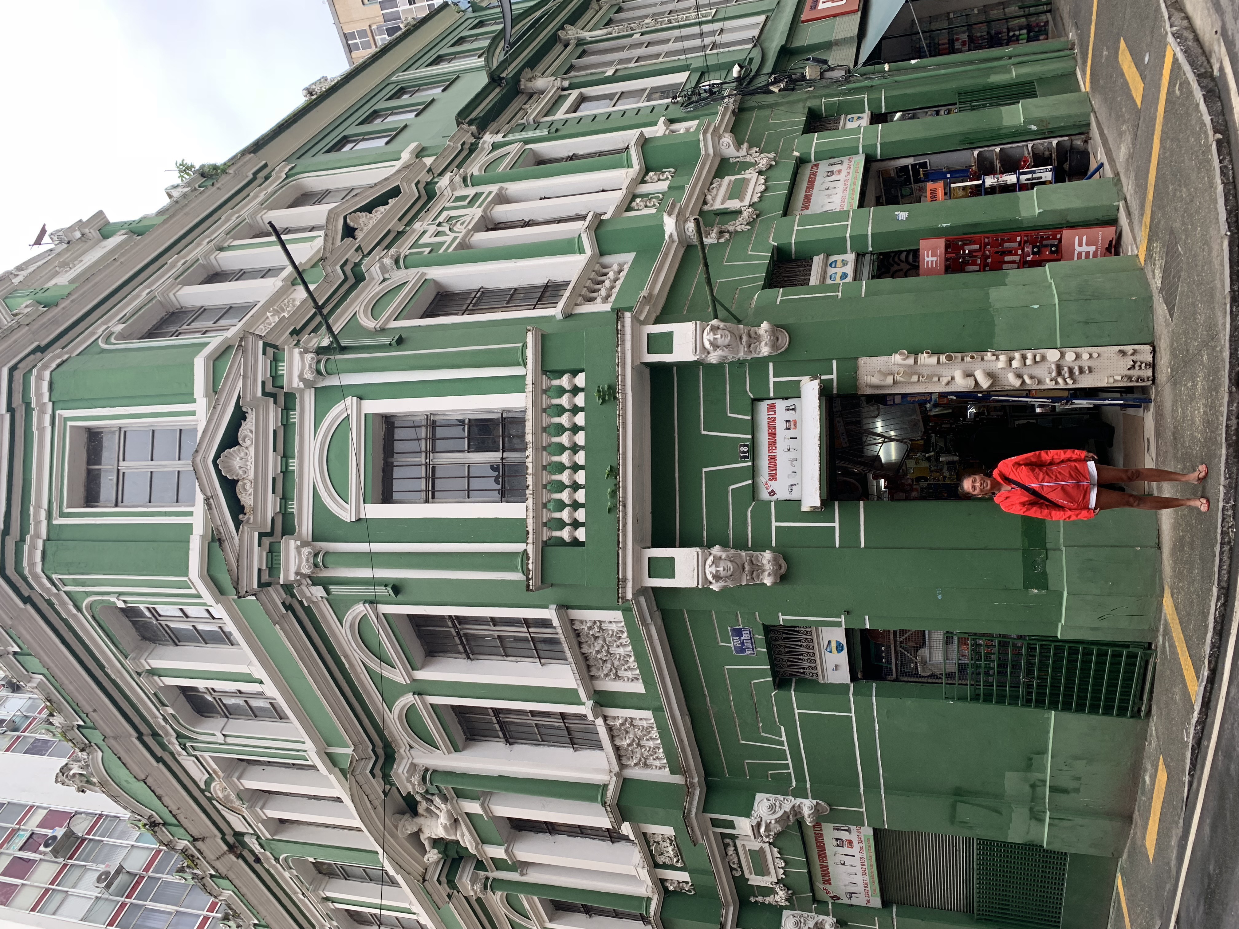 Yuka in her orange jacket in front of a magnificent green Art Nouveau corner building