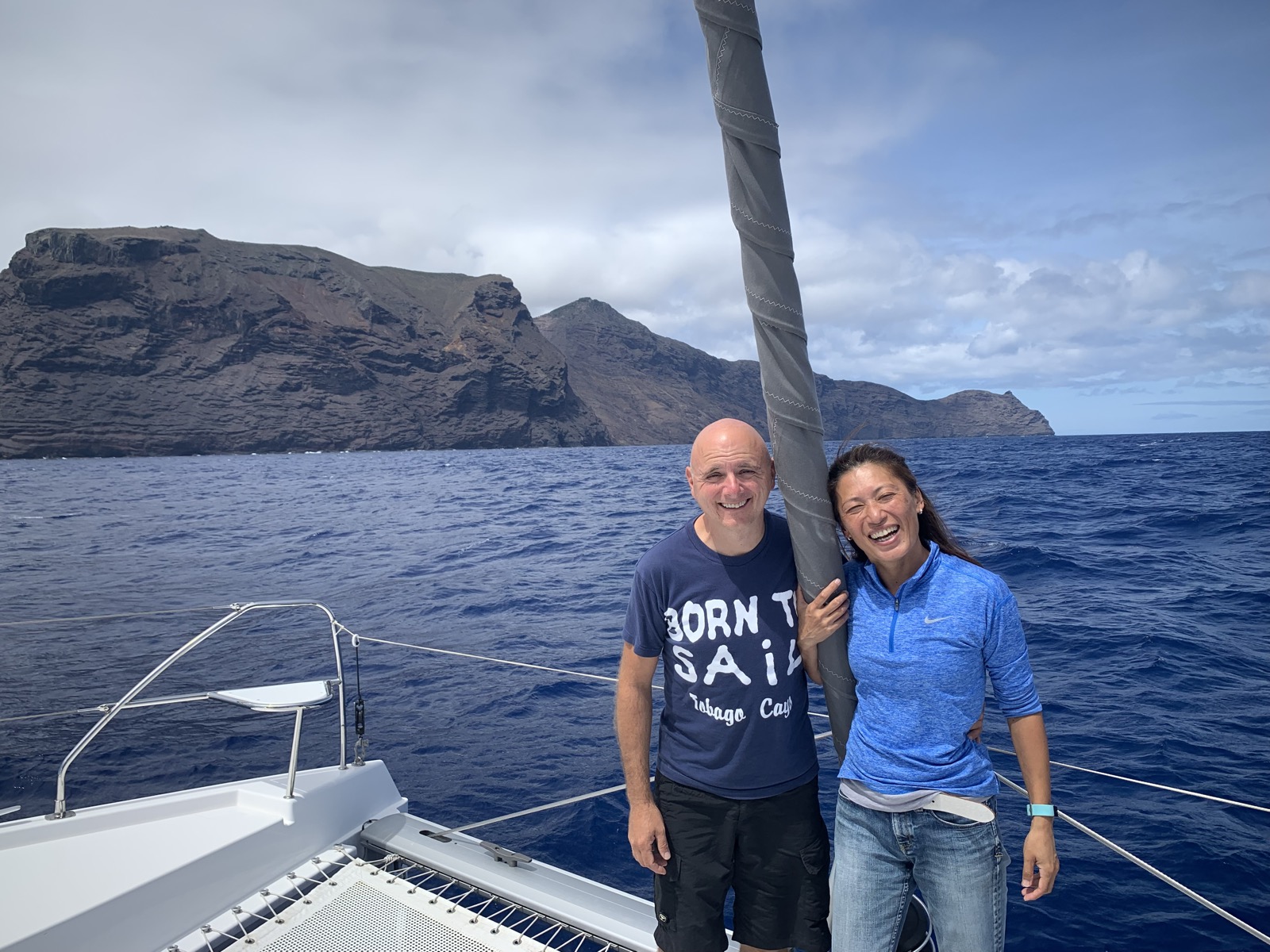 Francesco and Yuka on Oroboro's bow, St Helena's dramatic black volcanic cliffs towering behind them over deep blue ocean