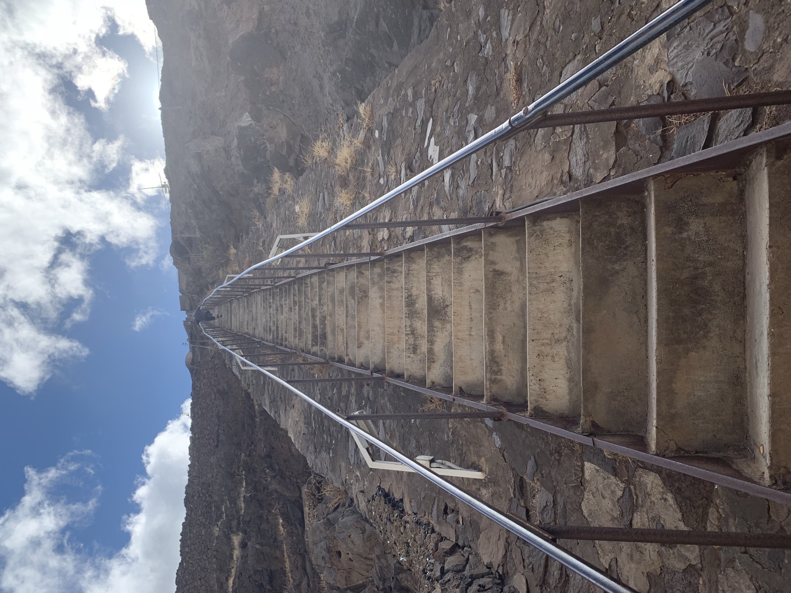 Jacob's Ladder viewed from below — concrete steps with metal railings climbing straight up the dark volcanic cliff face