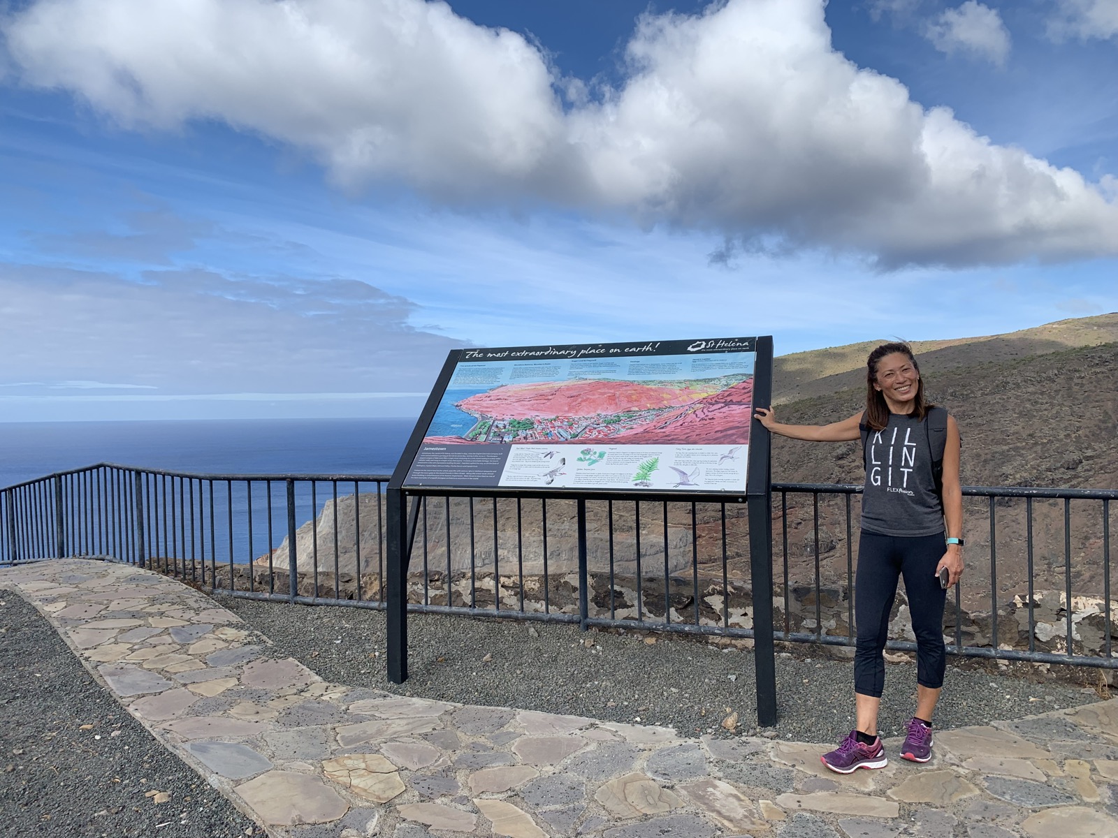Yuka at the top of Jacob's Ladder, next to the St Helena visitor information board reading 'The most extraordinary place on earth!'