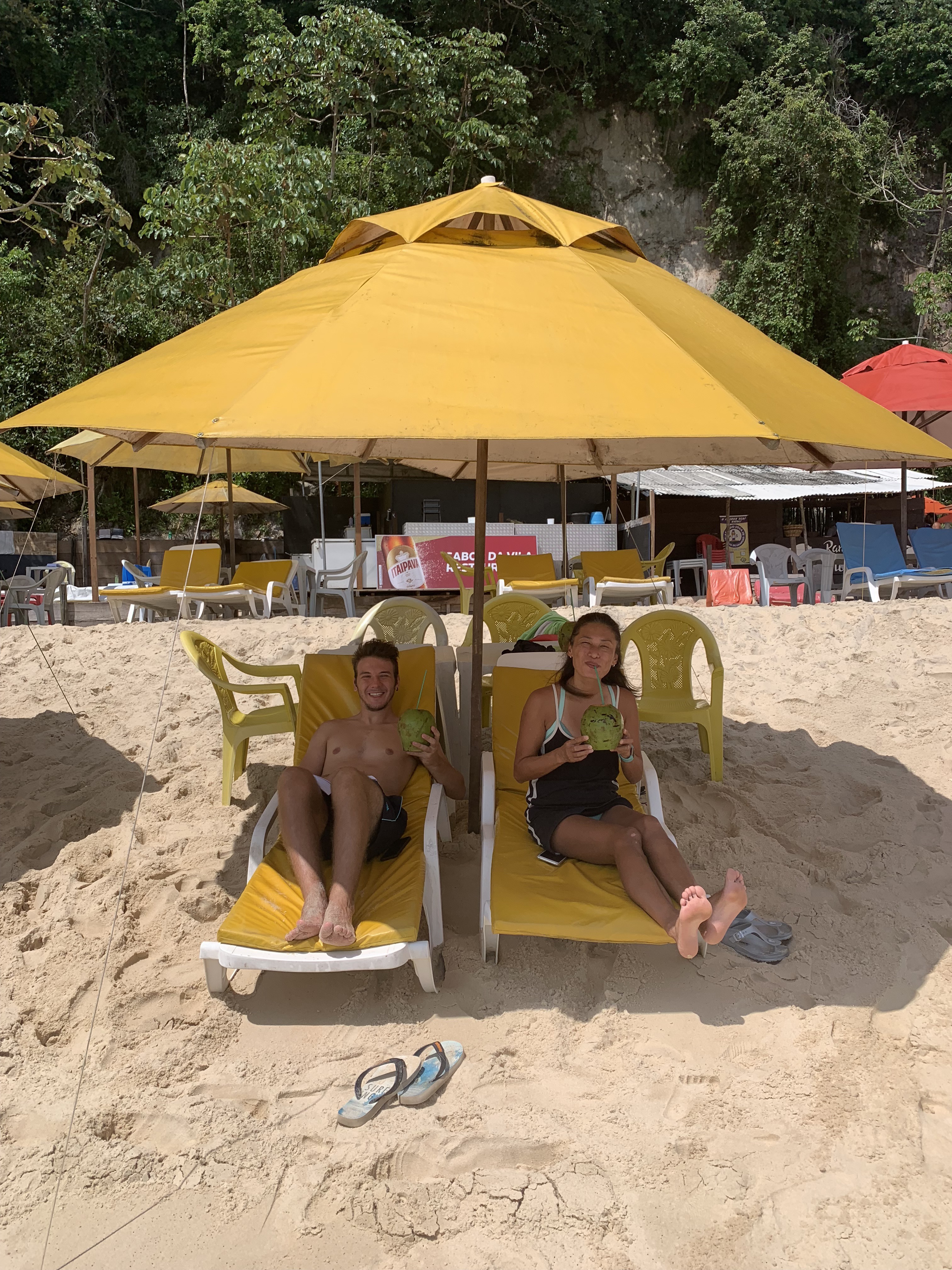 Yuka e Mario relaxando em uma barraca de praia sob guarda-sóis amarelos