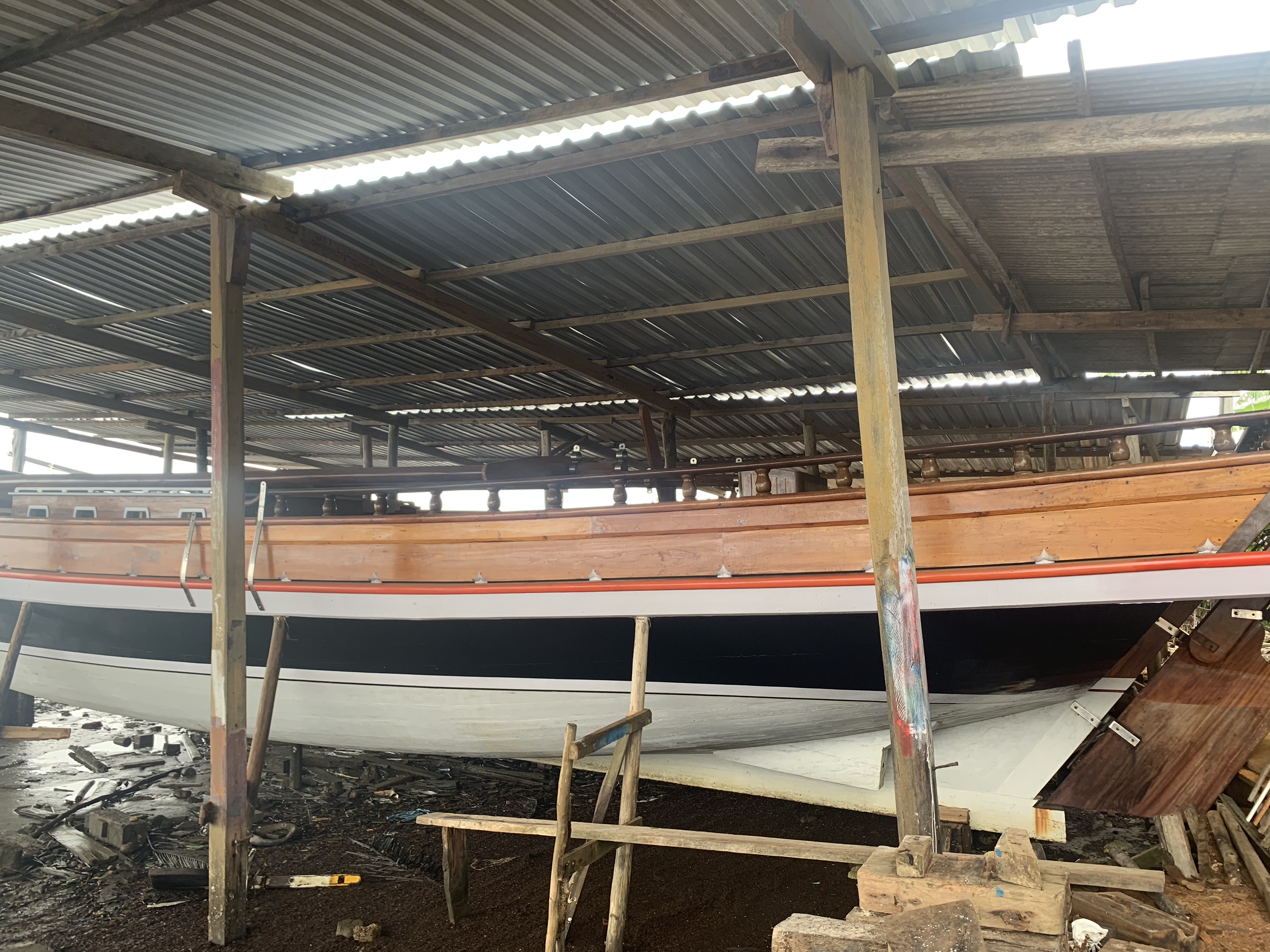 A newly built wooden boat under a covered shed, polished gunwale with bronze rivets, Camamu boatyard