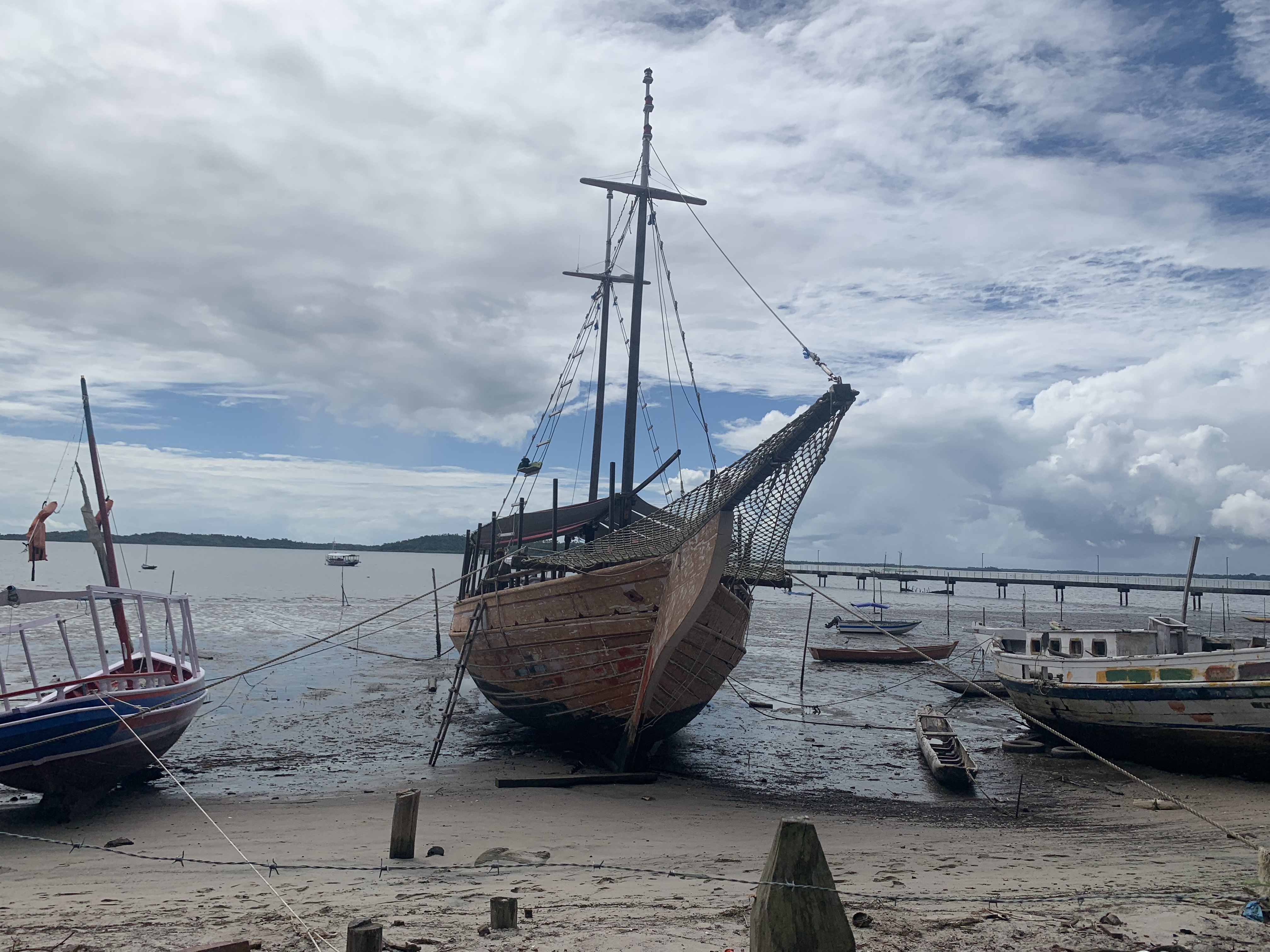 Full-sized replica of a Portuguese caravela beached at low tide in Camamu Bay, surrounded by working fishing boats